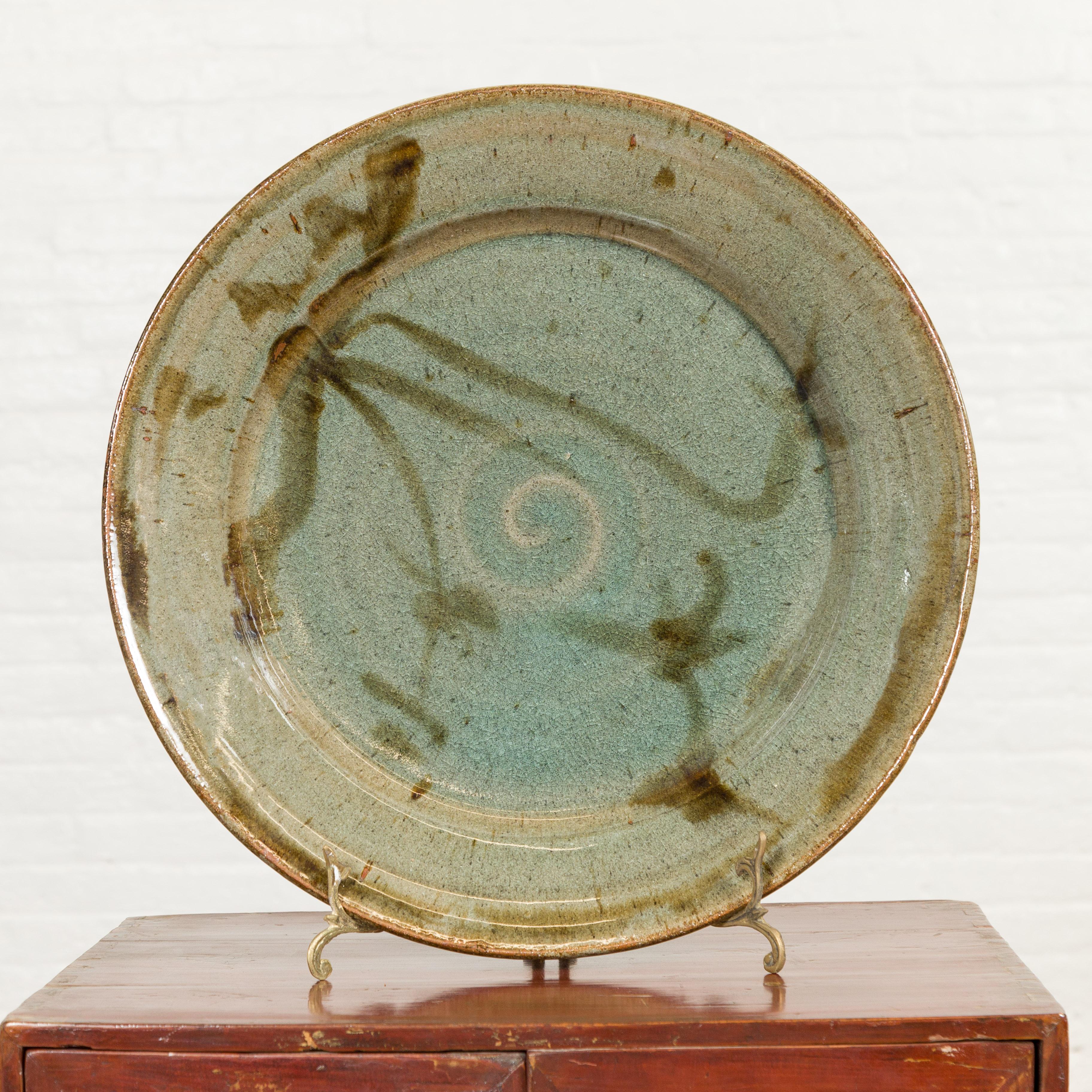 A contemporary Thai hand-thrown ceramic charger from Chiang Mai with hand painted decor. Created in Chiang Mai, Northern Thailand, this charger plate features a soft green hue perfectly contrasted to brown tones accents and adorned with a central