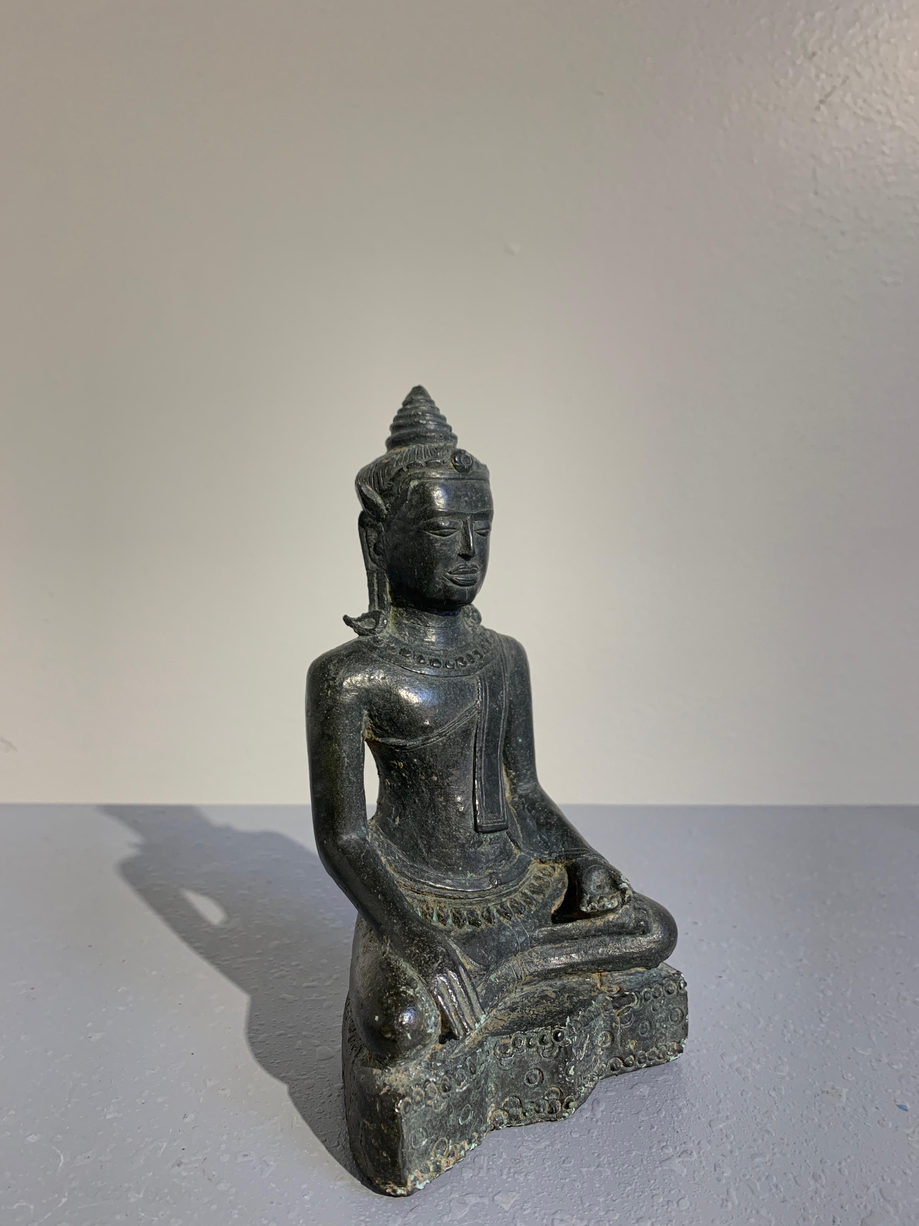A fine early Thai Lopburi figure of a crowned and adorned Buddha, cast bronze, mid-13th century.

The unusual figure of the Buddha sits in virasana upon a stylized lotus pedestal. He is dressed in the traditional monastic robes, but also adorned