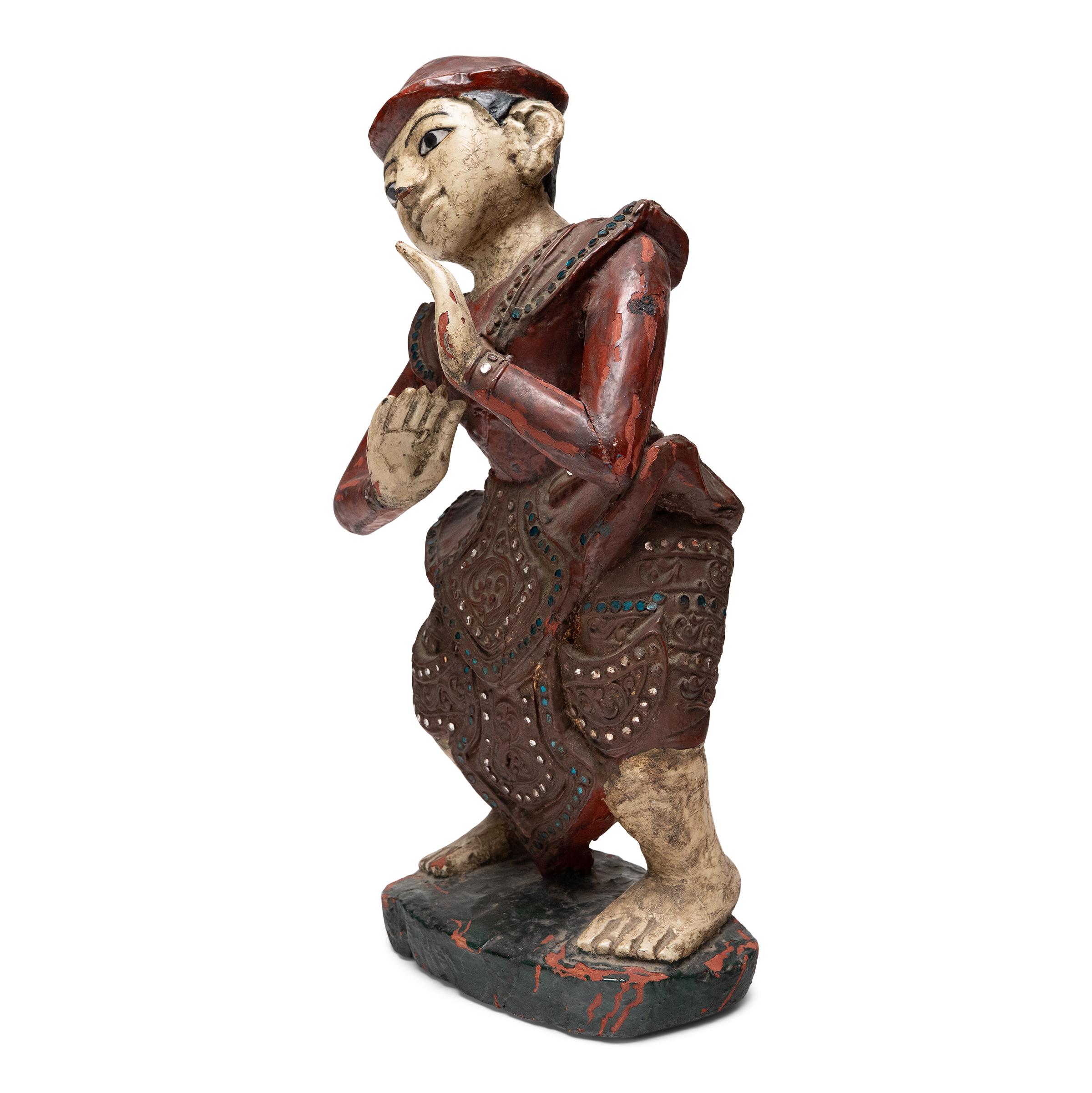Con le ginocchia piegate e il peso spostato su un lato, questa scultura tailandese dei primi del Novecento raffigurante un artista di corte è intrisa di movimento, come se stesse per scatenarsi in una danza tradizionale. La figura è un meraviglioso