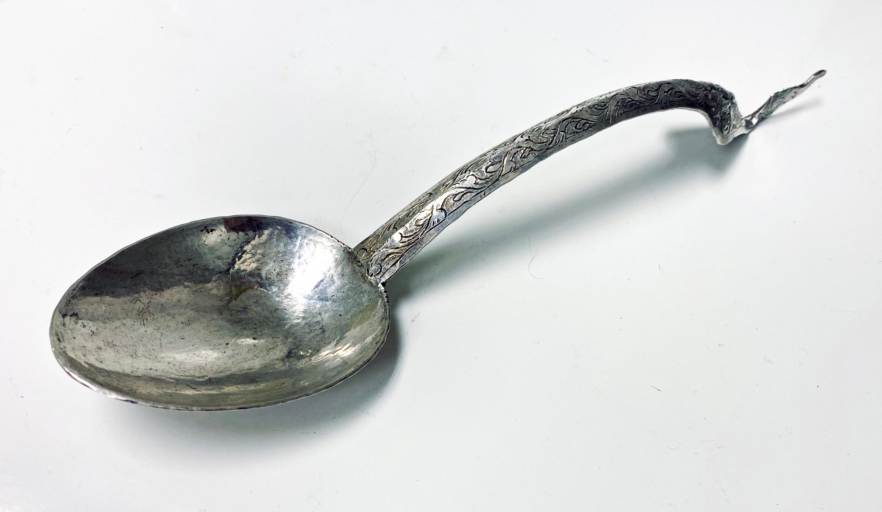 Thai silver rice serving ladle spoon. High grade, beaten silver ceremonial ladle. The long handle has an elongated lozenge shape with a stylised flame or dragon like motif finial. The bowl of the spoon is oval shaped. The front of the handle and