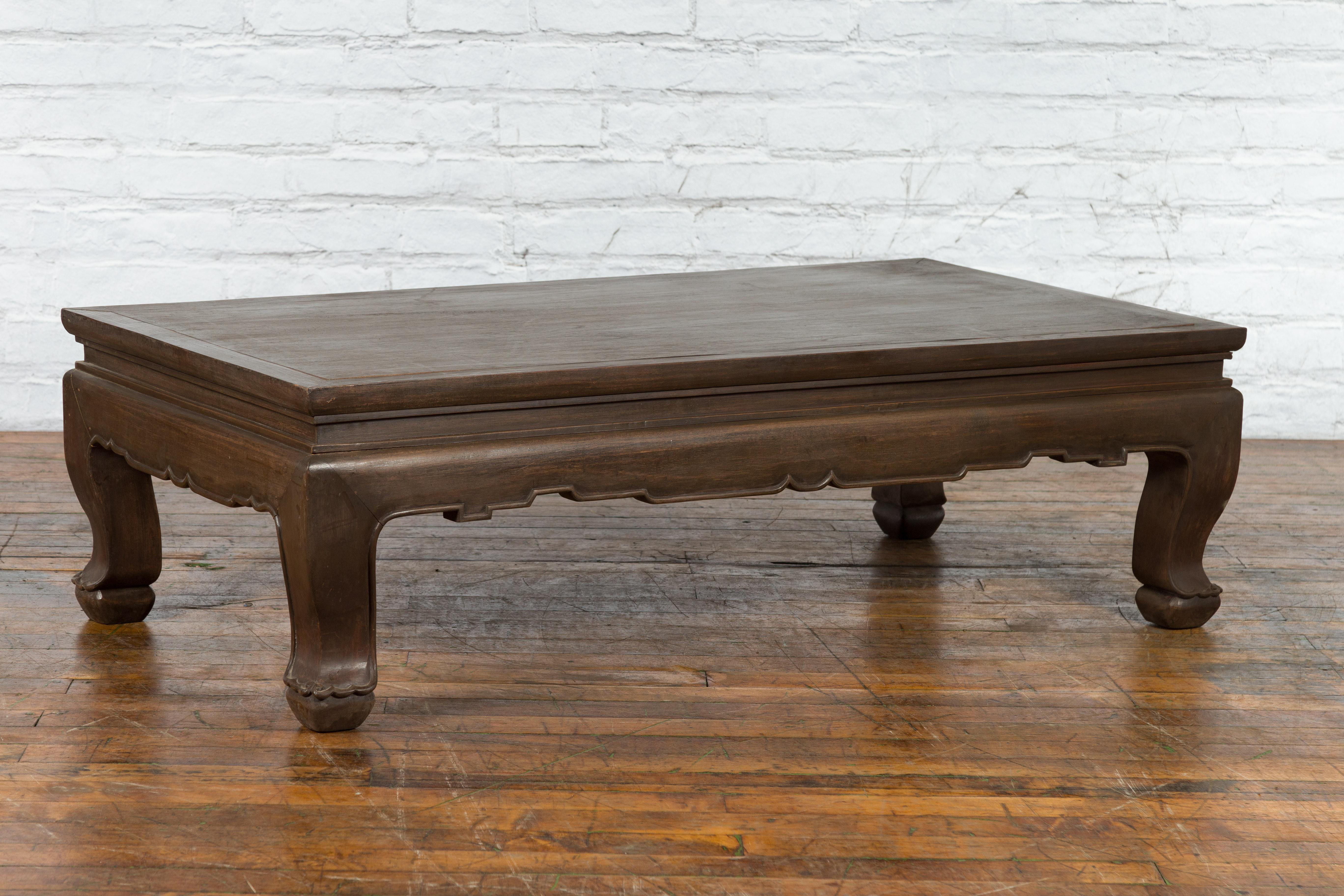 A vintage Thai teak wood coffee table from the mid 20th century with carved apron, cabriole legs, brown patina and petite feet. Created in Thailand during the Midcentury period, this teak wood coffee table features a rectangular top with central