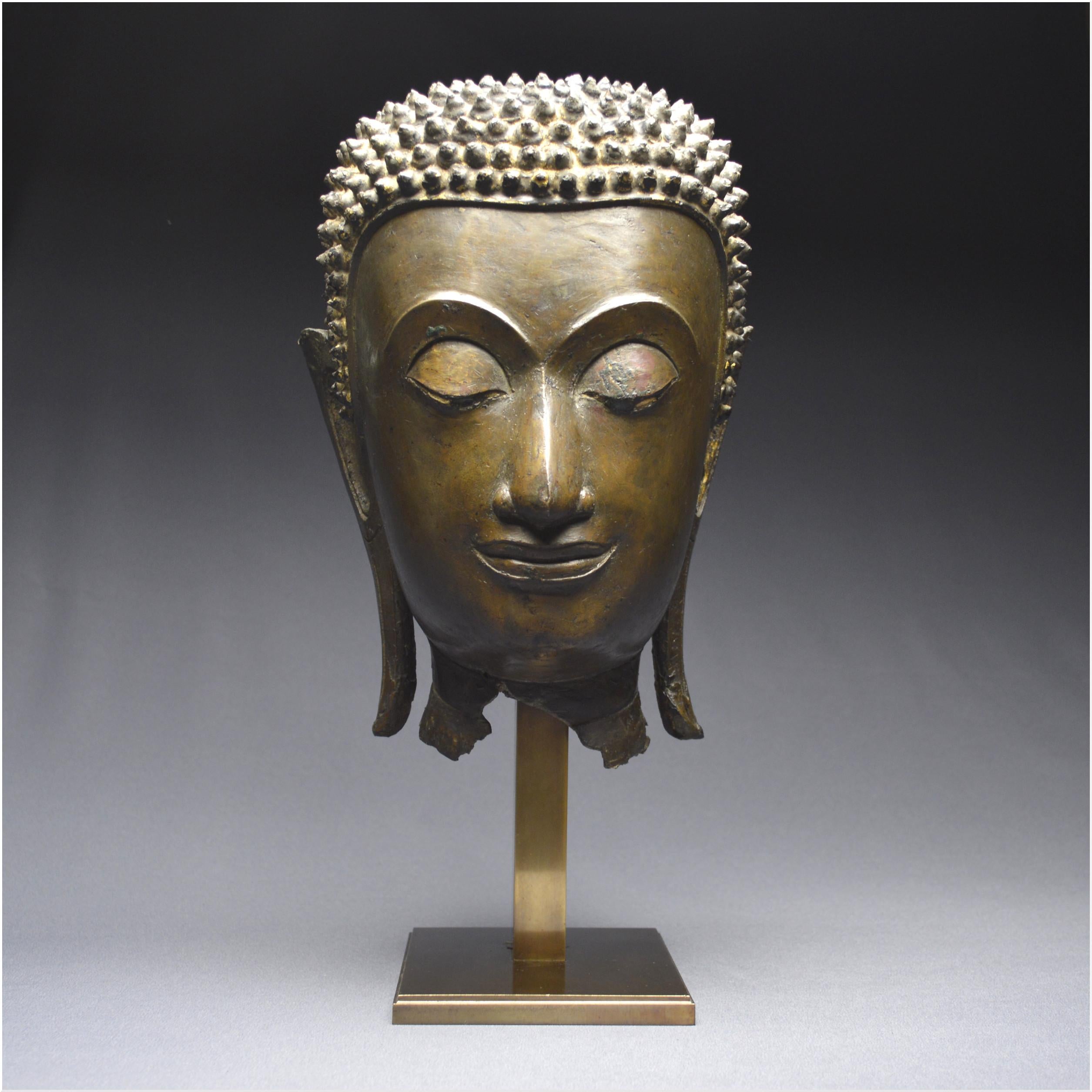 Large bronze Buddha head
Ancient Kingdom of Siam
Ayutthaya School
16th - 17th century

The very soft face is set in an oval and is characterized by fine curvilinear brow ridges with perfect curvature meeting at the base of the an aquiline nose with