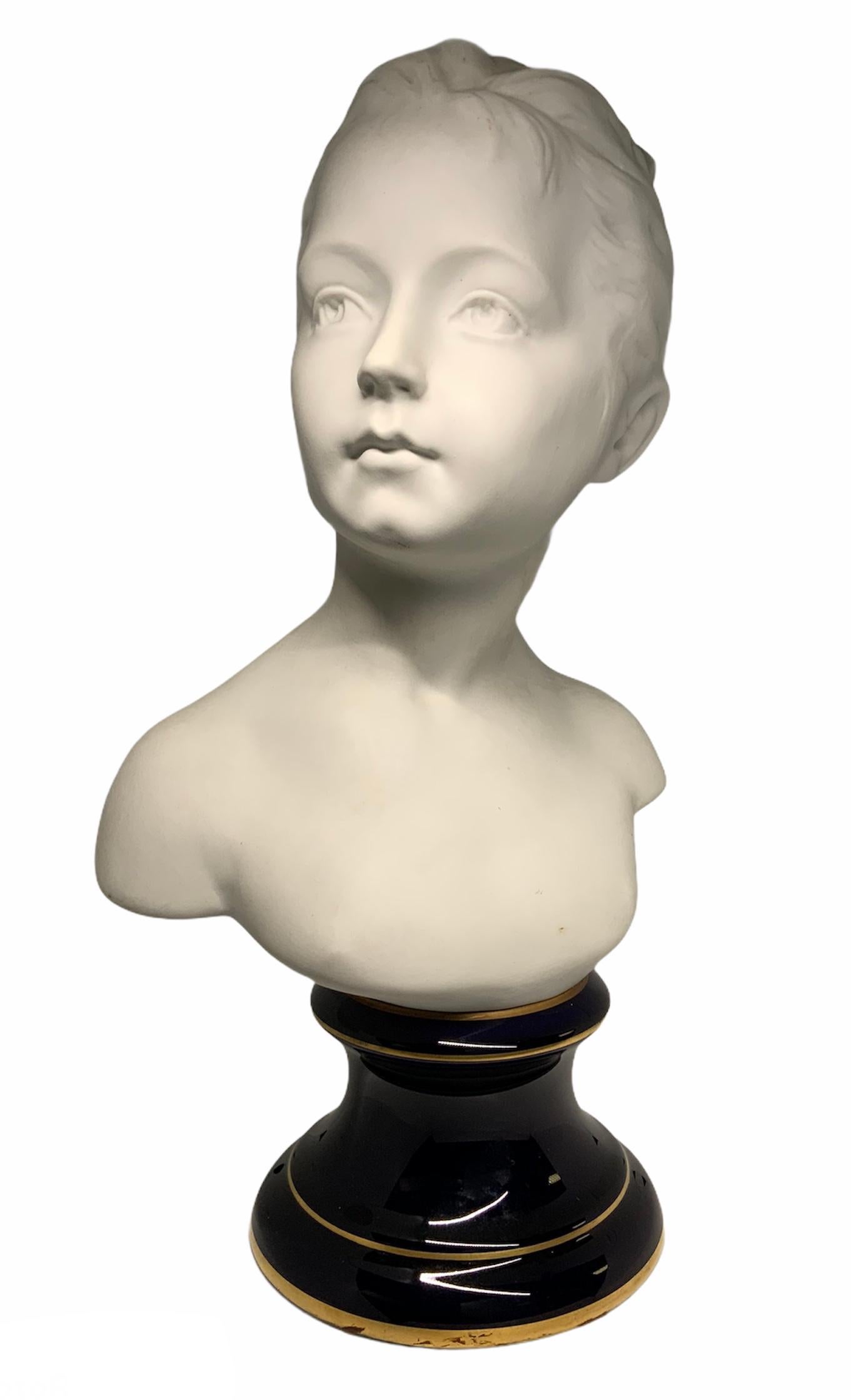 This is a white bisque porcelain large bust of a girl. Her hair is adorned with a bow and ribbon. The bust stands over a gilt border cobalt blue pedestal base. Under the base is written in gold Porcelanas Tharaud, Limoges France.