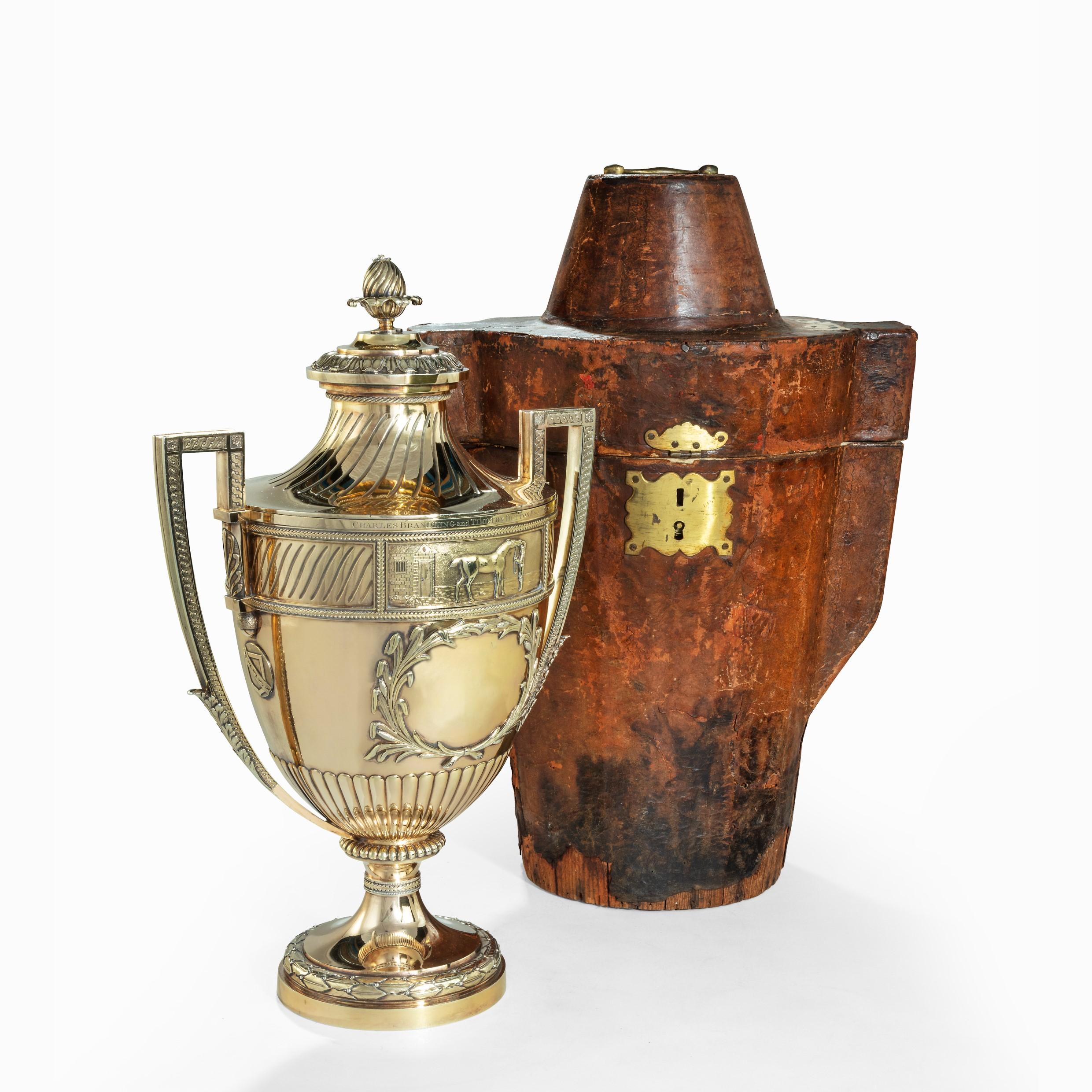 This exceptional silver-gilt trophy was made by Paul Storr in 1802, by arrangement with the London retailer Robert Makepeace. It is in the form of a classical footed cup with squared handles and separate shaped cover. It is embossed, chased and