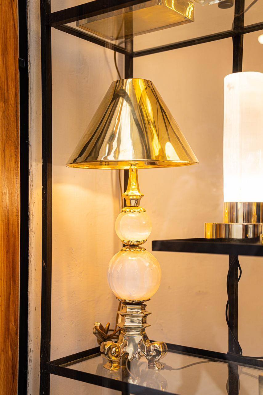 The Agadir Lamp is composed of a golden brass lamp shade which rests upon two ochre selenite spheres. The crystal spheres then sit on a triangular shaped brass base consisting of 3 legs. This lamp adds a touch of sophistication and warmth to any