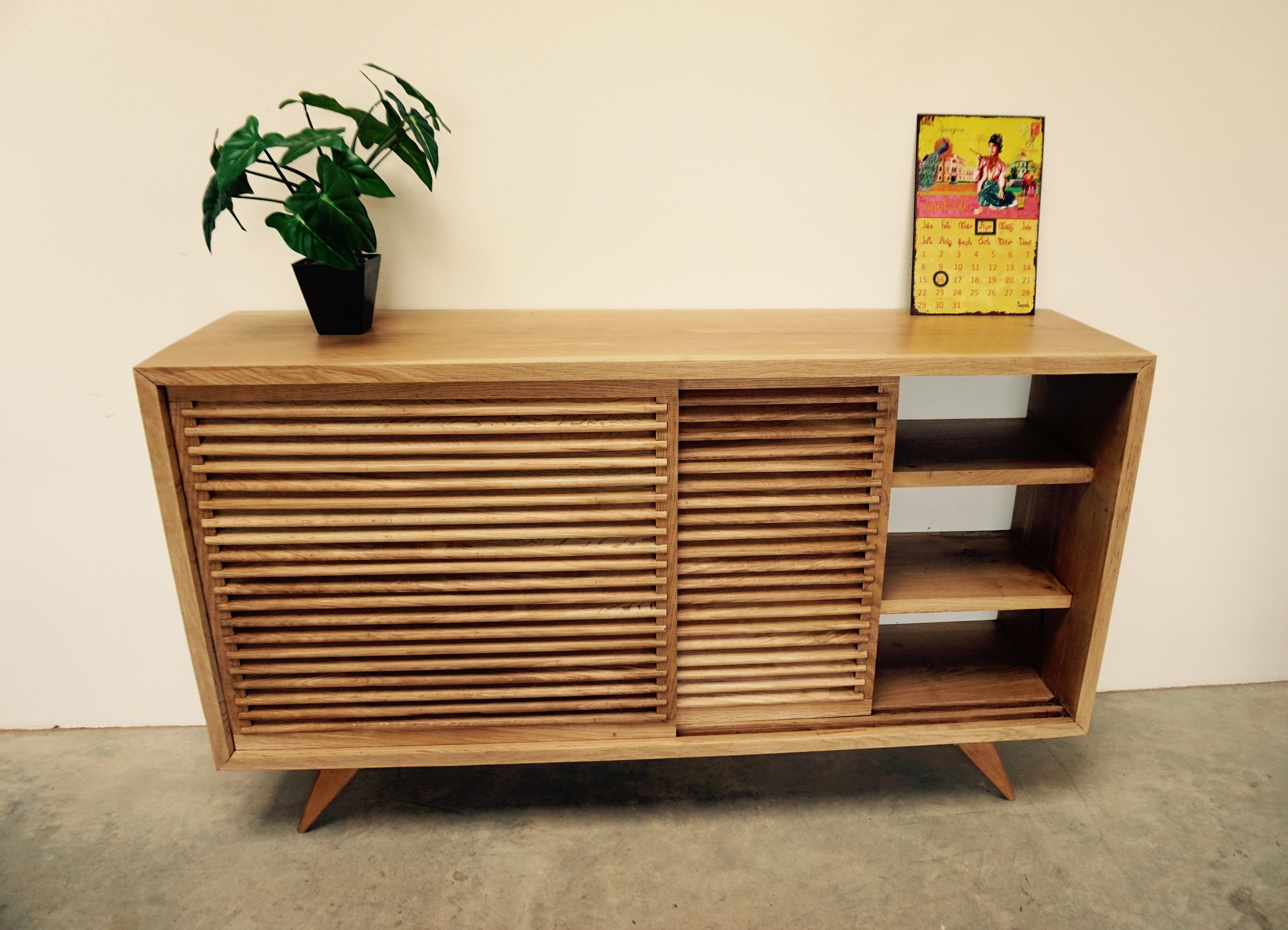A solid Oak sideboard with two central sliding doors that are comprised of multiple rounded slats, uniformly spaced at a downward facing angle. They have an easy sliding system in order to enable smooth functionality. Resembling European shutters of