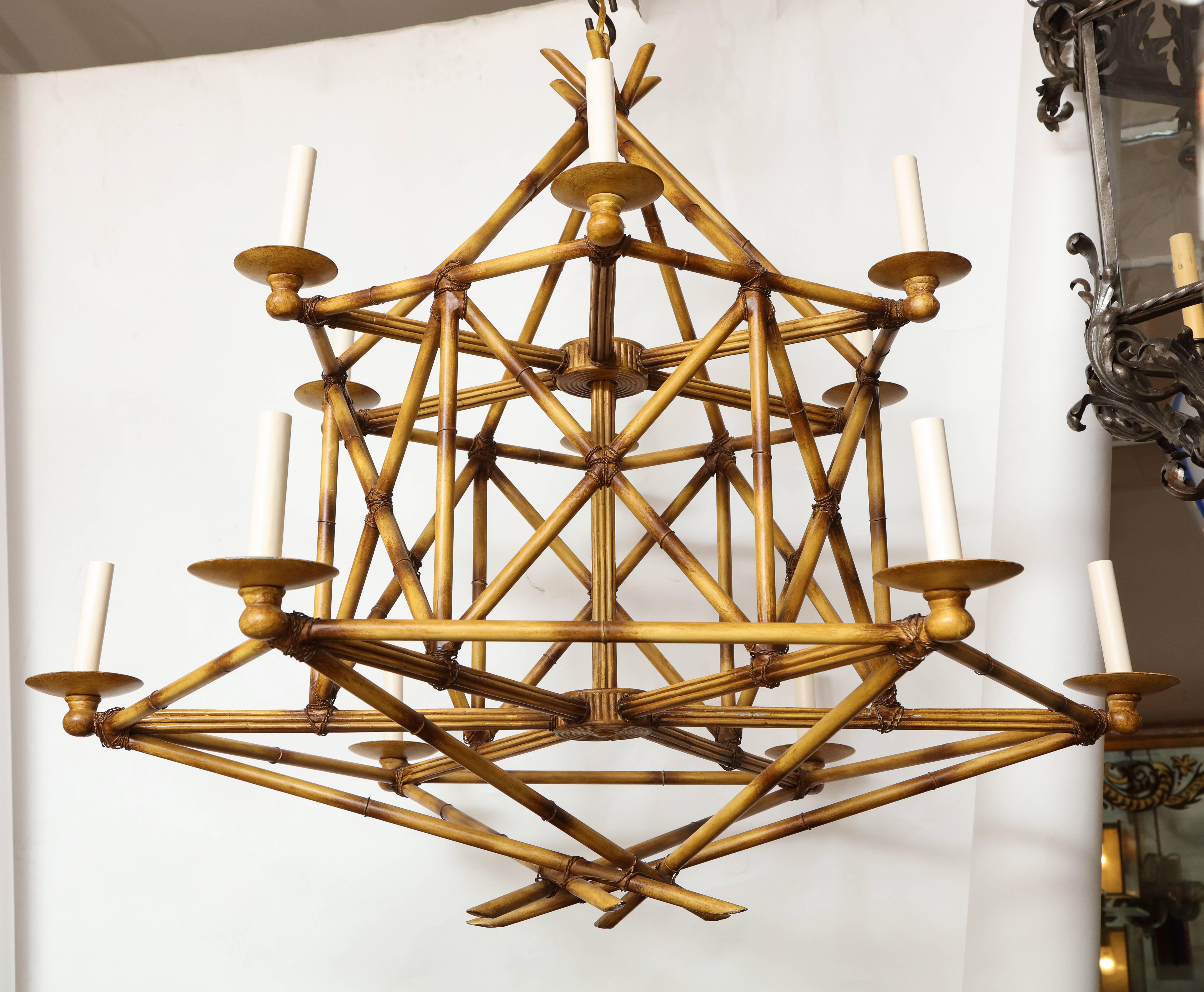 A twelve light, two-tiered faux bamboo chandelier. Featuring an intricately constructed cage, formed by cross-banded sections of hand-painted faux bamboo made from brass, with bobeches issuing twelve candles sleeves for a warm, glowing effect.