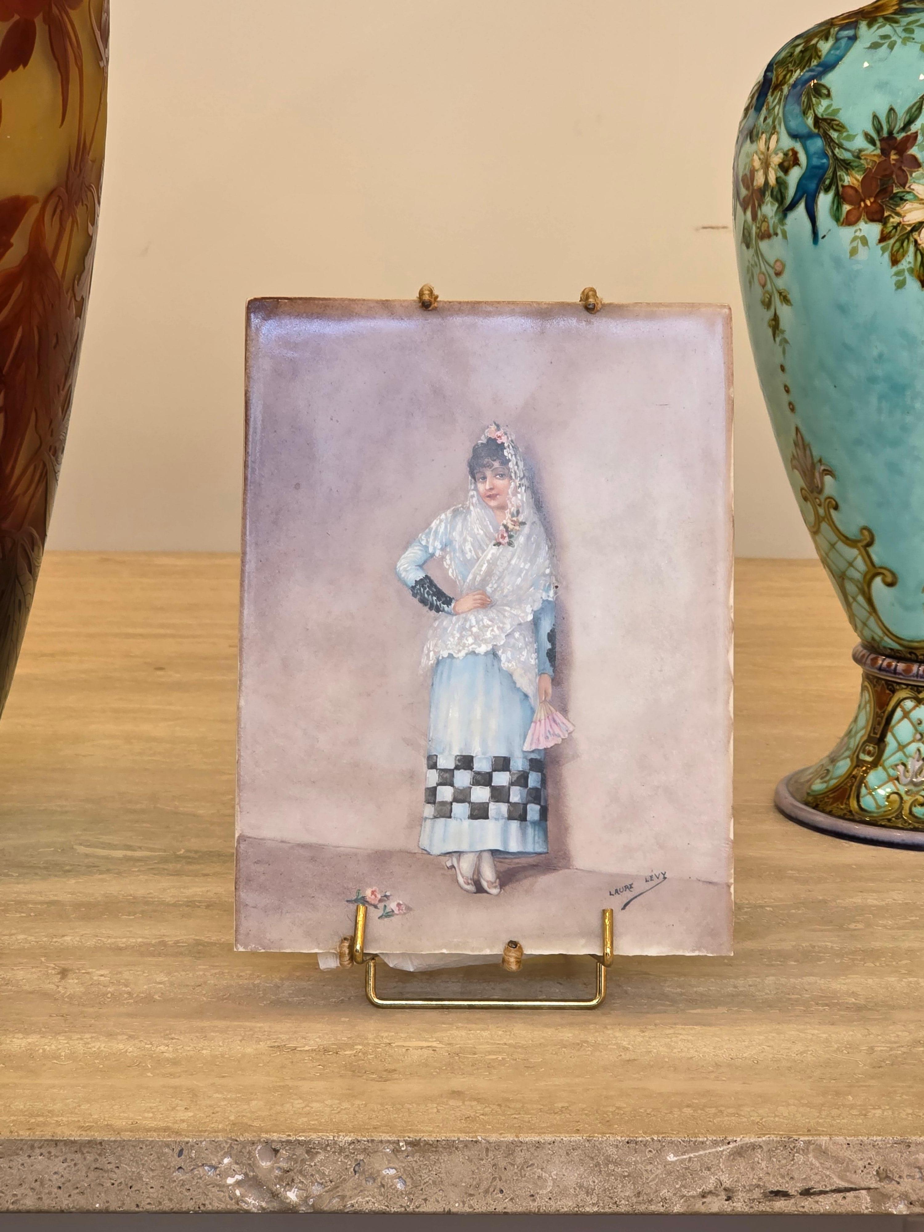 Laure Levy (1866-1954)
The Beautiful Andalusian
Hand-Painted Polychromed Porcelain Plaque 
Depicting an Andalusian woman in traditional dress, leaning against a wall, a fan in her hand, a few roses strewn in front of her.
Signed lower right

Laure