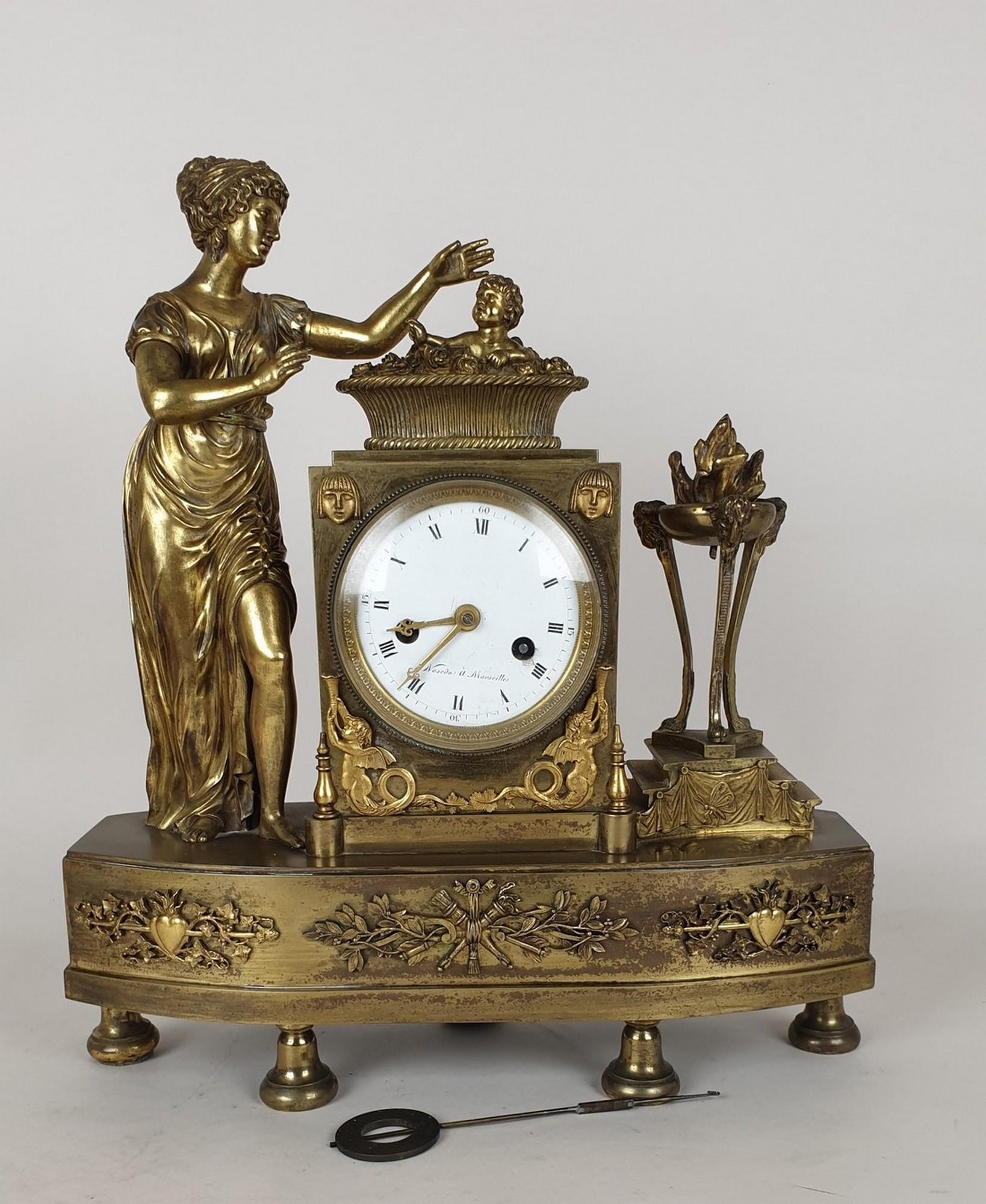 Patinated bronze clock representing The Birth of the King of Rome or the allegory of the Birth of Love

Empress Marie-Louise is standing near a cradle filled with roses with a winged cupid in the middle; decor of an Athenian woman with rams' heads