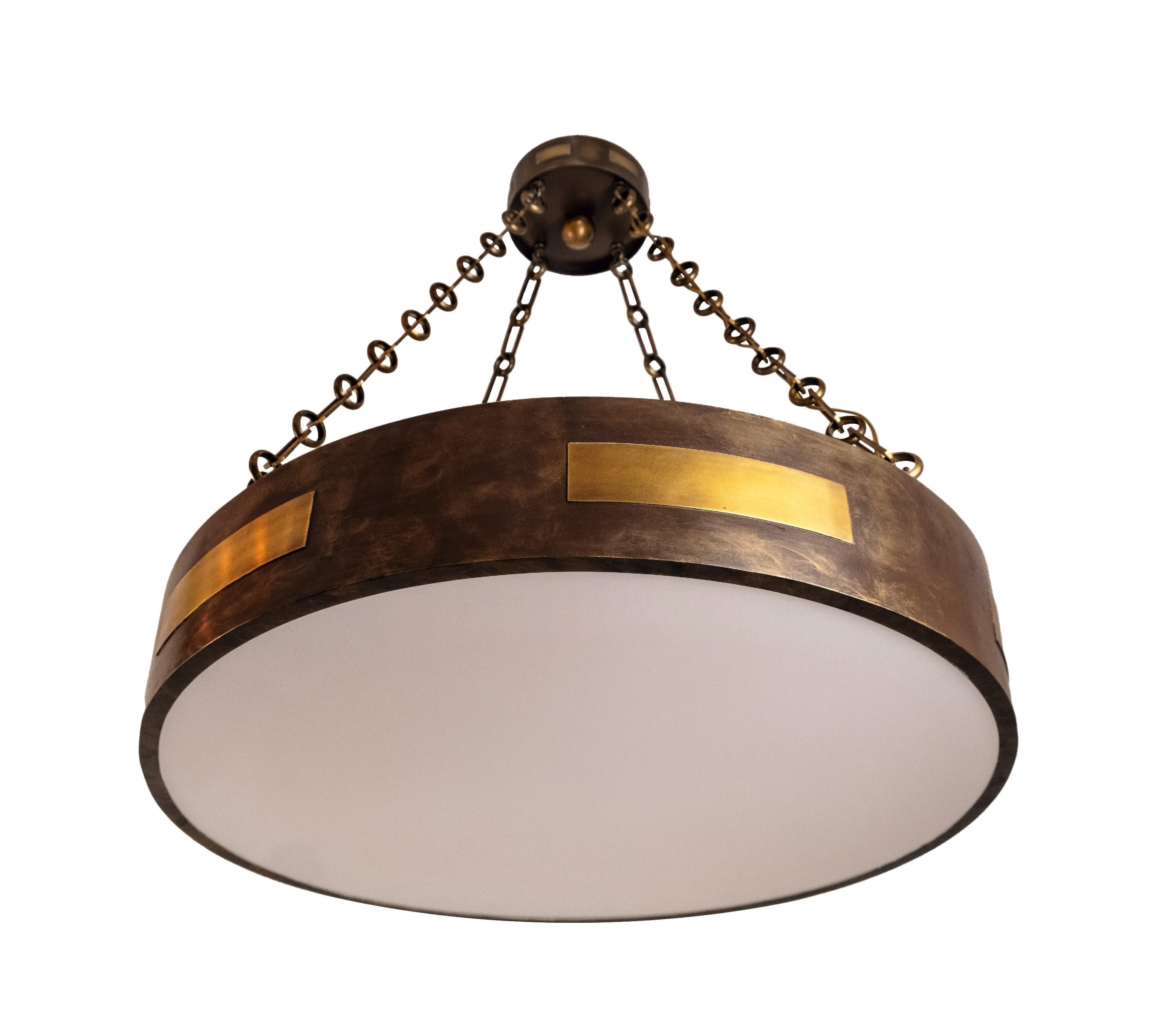 A round, single-tiered pendant light with a patinated chocolate brown finish and patinated brass horizontal panels on the dish and canopy. The dish suspended by three links of brass chain, and having an opal plexi diffuser, concealing 4 medium