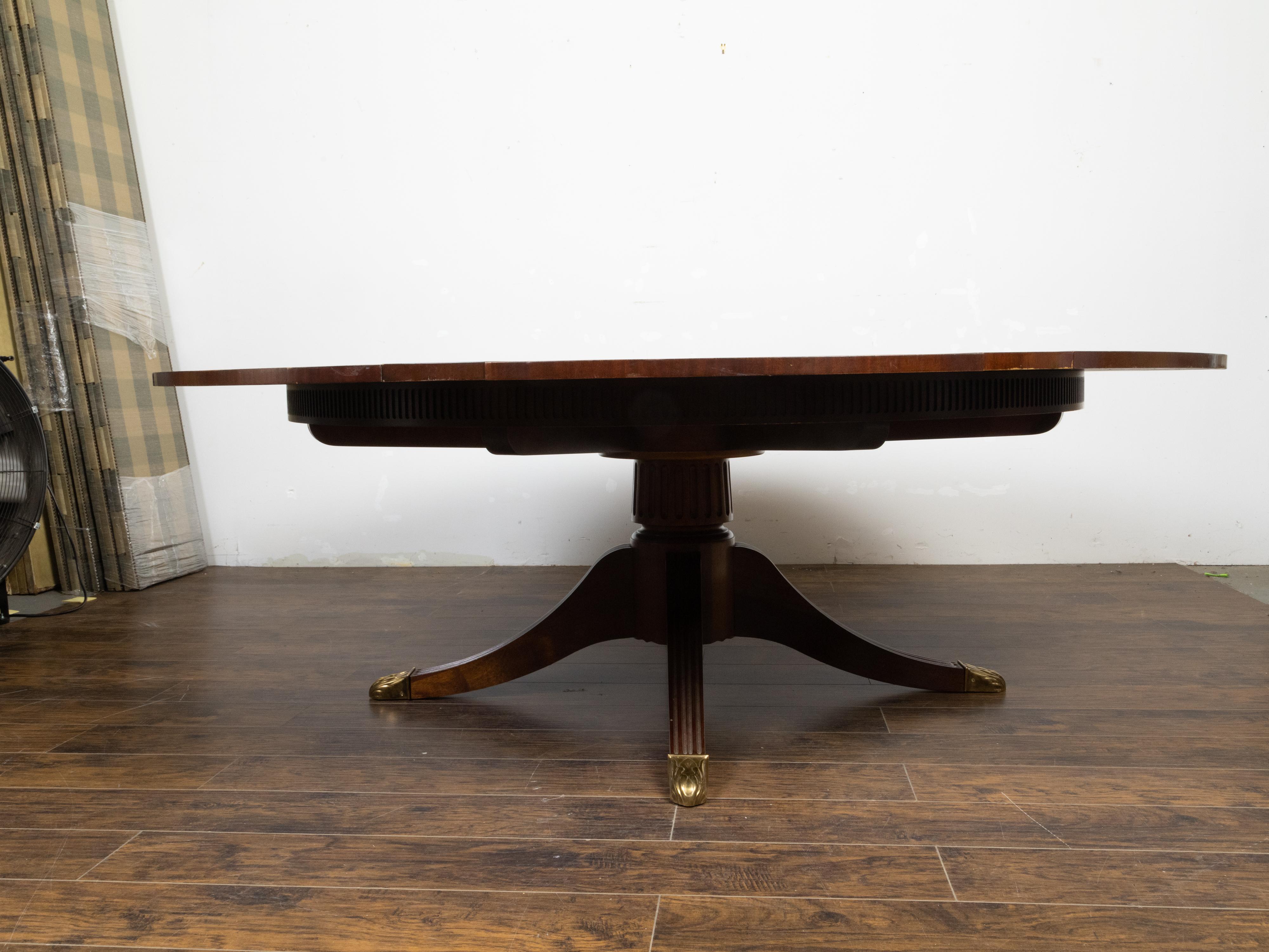A vintage Regency style mahogany extending dining table by Baker Furniture Company called the 'Capstan', part of the Stately Homes Collection from the late 20th century, with round swirling mahogany top, gilded brass tips, pie-crust style apron and