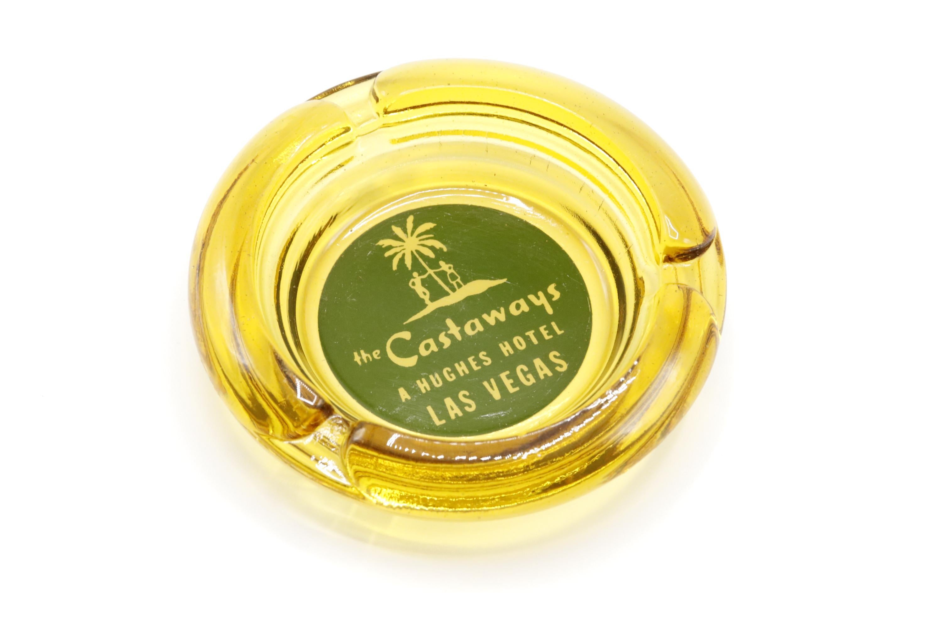 A yellow glass ashtray from The Castaways Hotel, a hotel and casino in Paradise, Las Vegas, Nevada. The center is printed with a green circle branded with the Castaways logo. The hotel, permanently closed in 1987, was opened in 1963 and purchased in