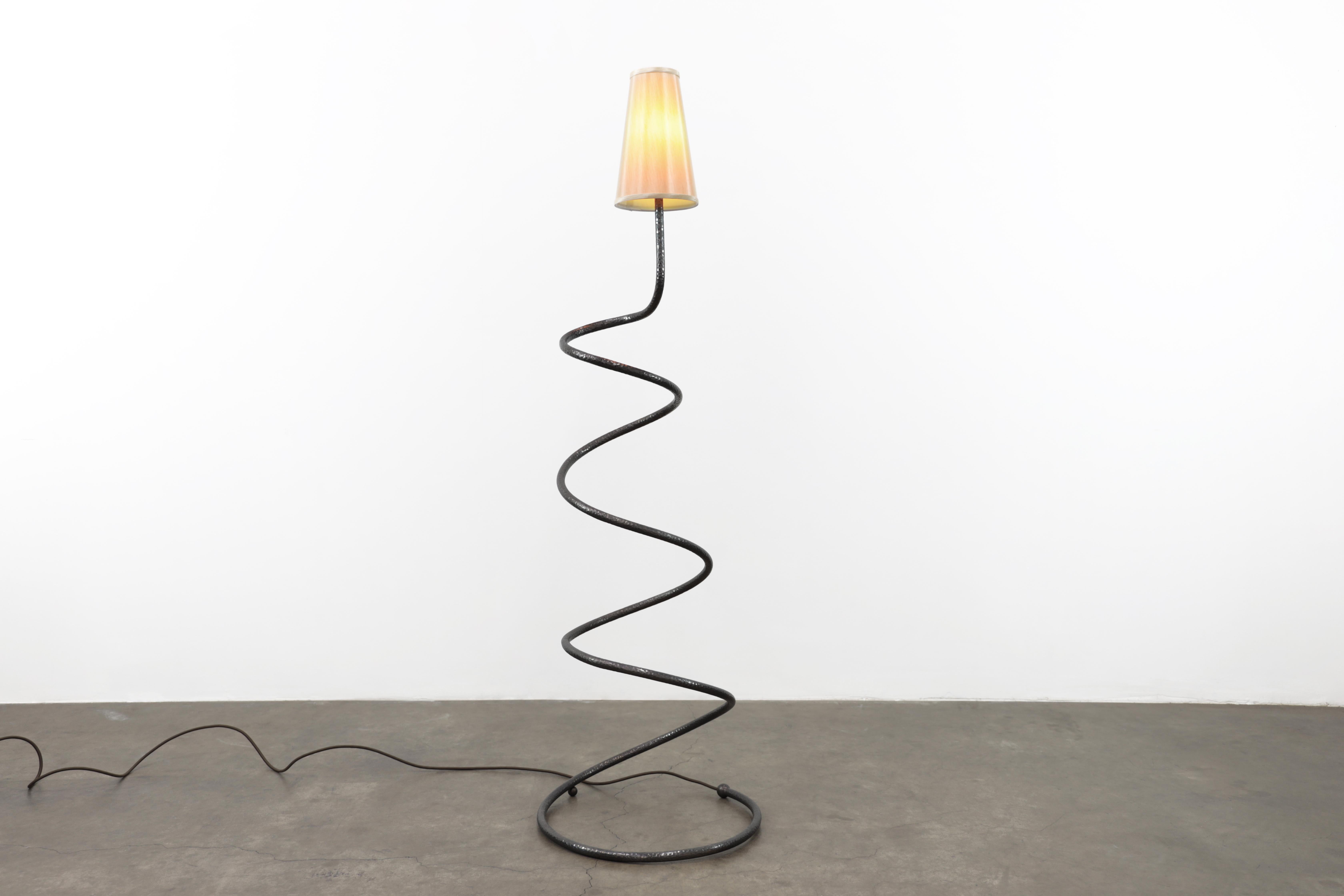 The Comet floor lamp is sure to bring joy to any environment. It's sculptural form is more than a perfect spring which makes it fun. The body of the lamp is hand hammered brass in an oiled bronze patina. The lampshade is silk. There is a dimmer on