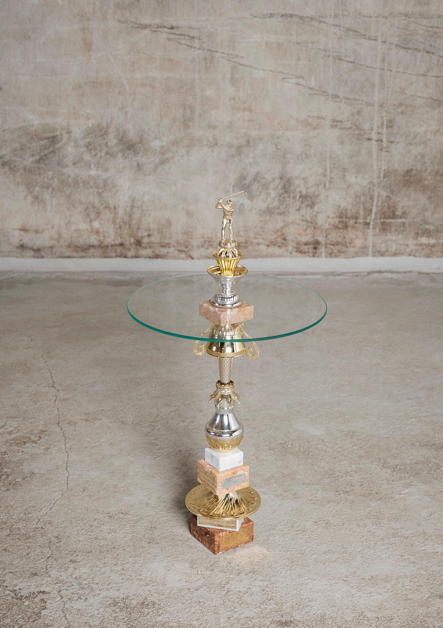 The Crown table by Flétta
Dimensions: 76 x 54.5 cm
Materials: gold, silver, pink marble

Trophy is a collection of tables, lights, flowerpots and shelves made of old trophies collected from athletes and sports clubs in Iceland. Trophies are a