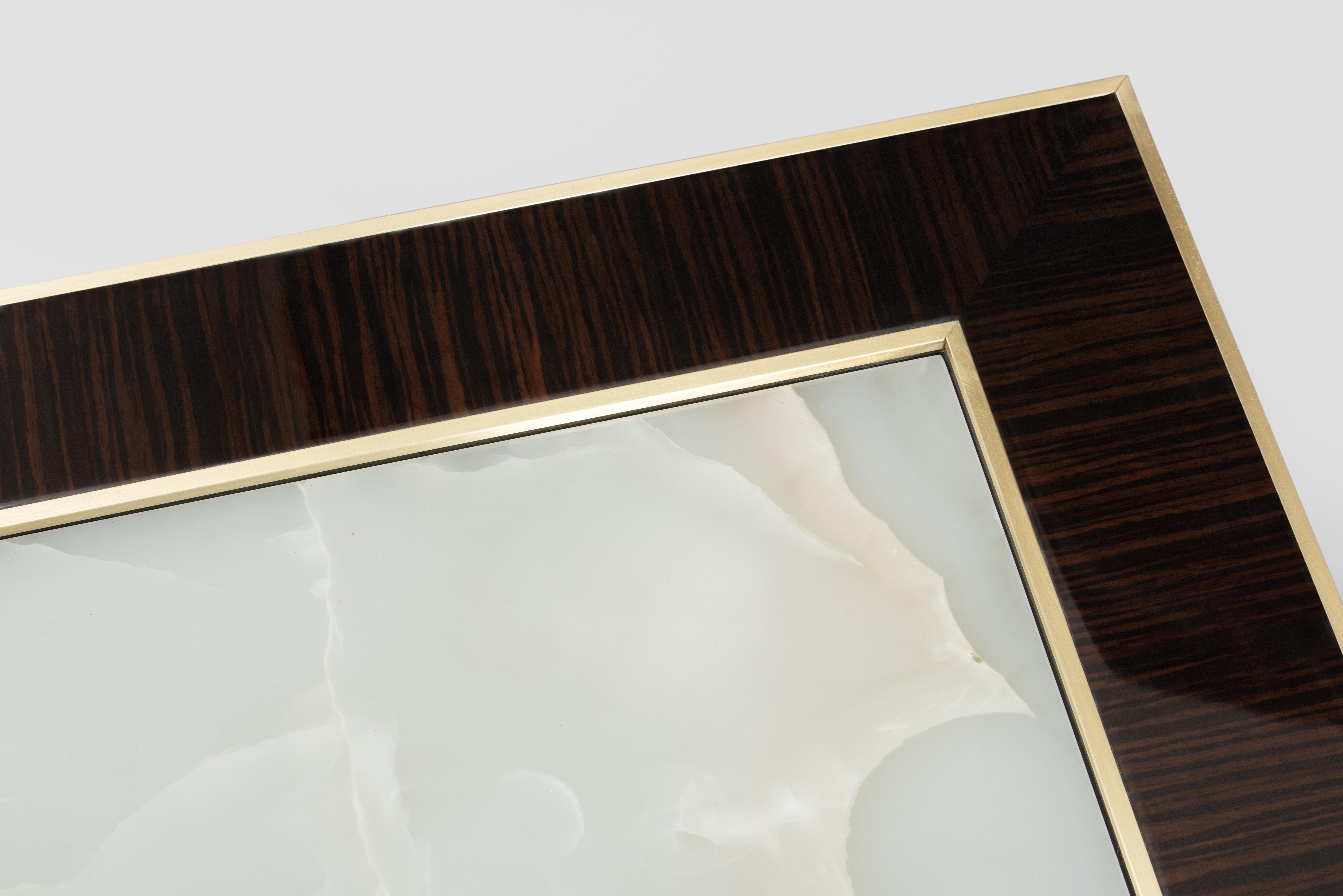 The side table is a piece with a warm, golden hue. The table top is made from honey onyx, a natural stone that has a beautiful, translucent quality and rich, warm colors. The onyx top is framed by a polished macassar ebony border with brass inlay,