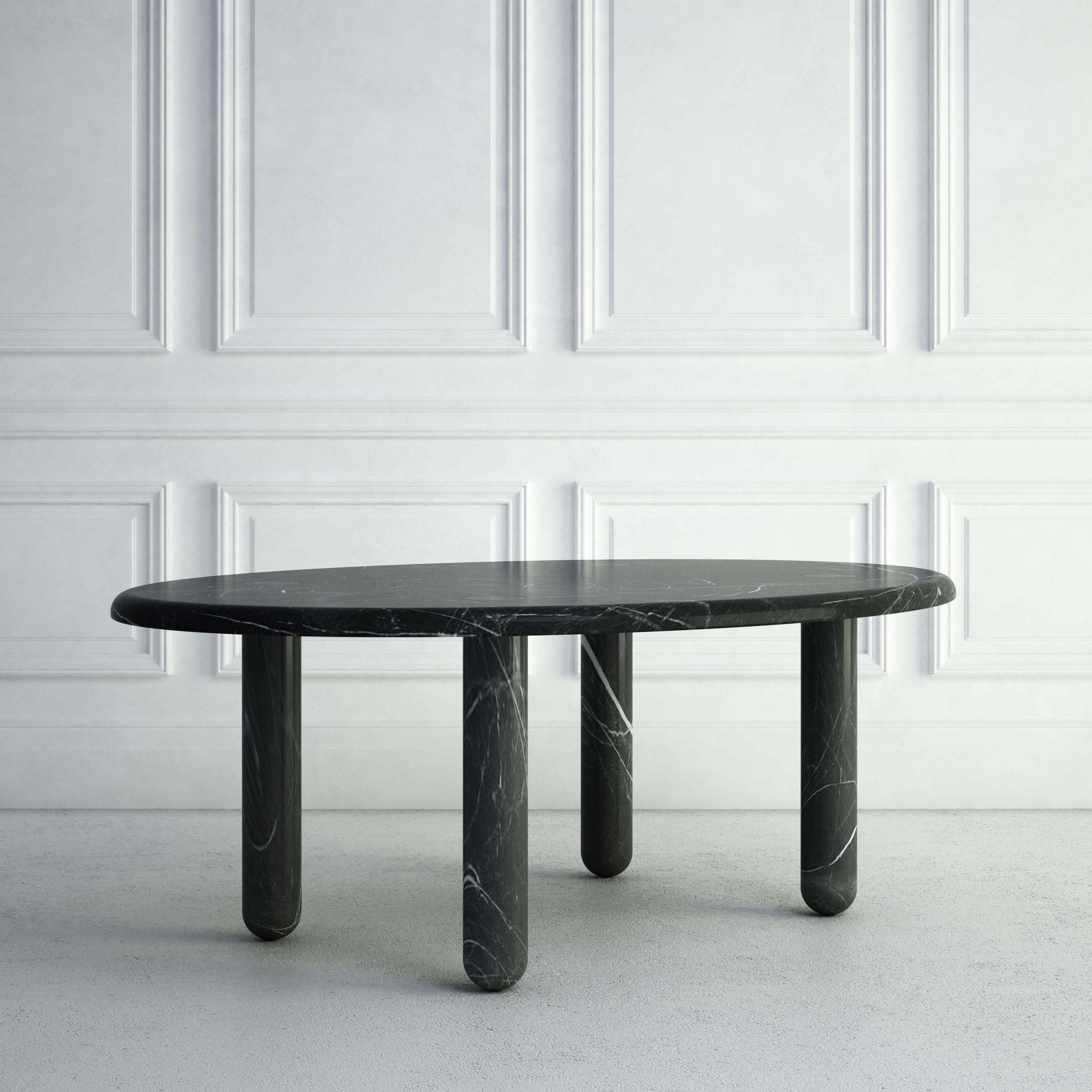 The Delphine is a graceful modern dining table. The top is a carved oval-shaped stone slab, with subtle edging. Each of the four legs is carved into a thin, cylindrical shape, with the bottoms of the legs gently rounded. This gives the table a very