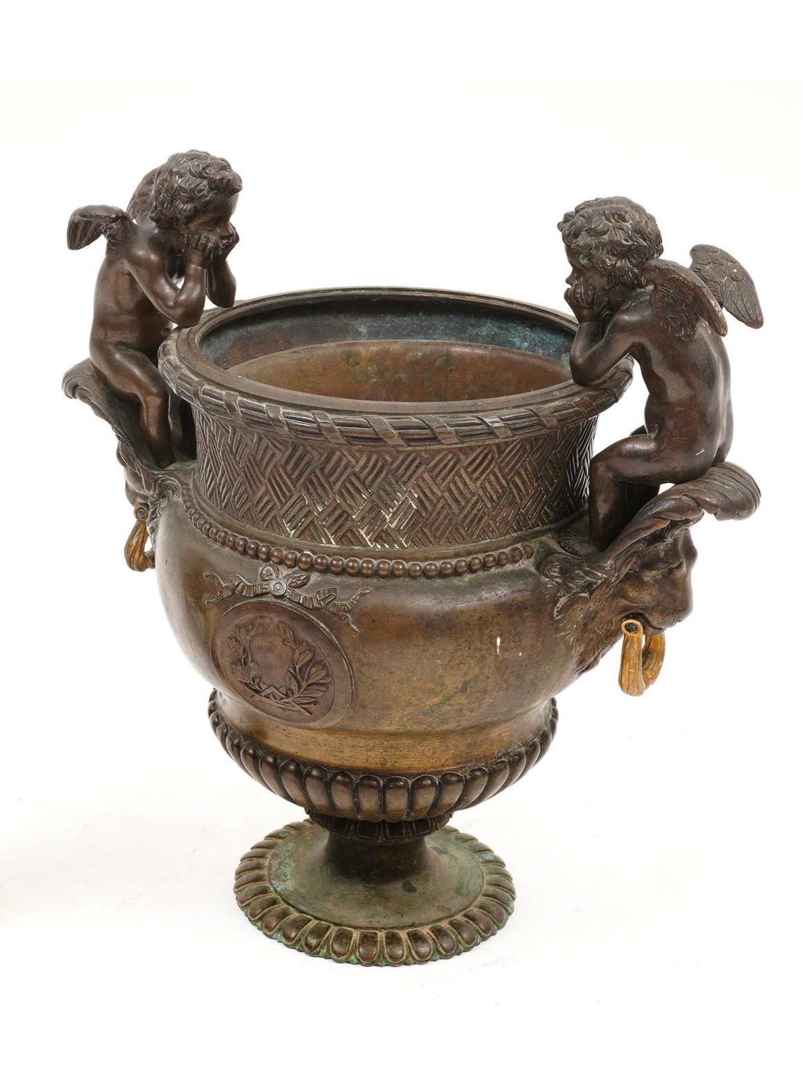 Beautiful patinated Belle Epoque cast bronze urn featuring two seated cherubs over lion mask handles, foliate medallions and garland. The urn is believed to be designed by artist Pierre Duval Le Camus. It is in great condition and has excellent