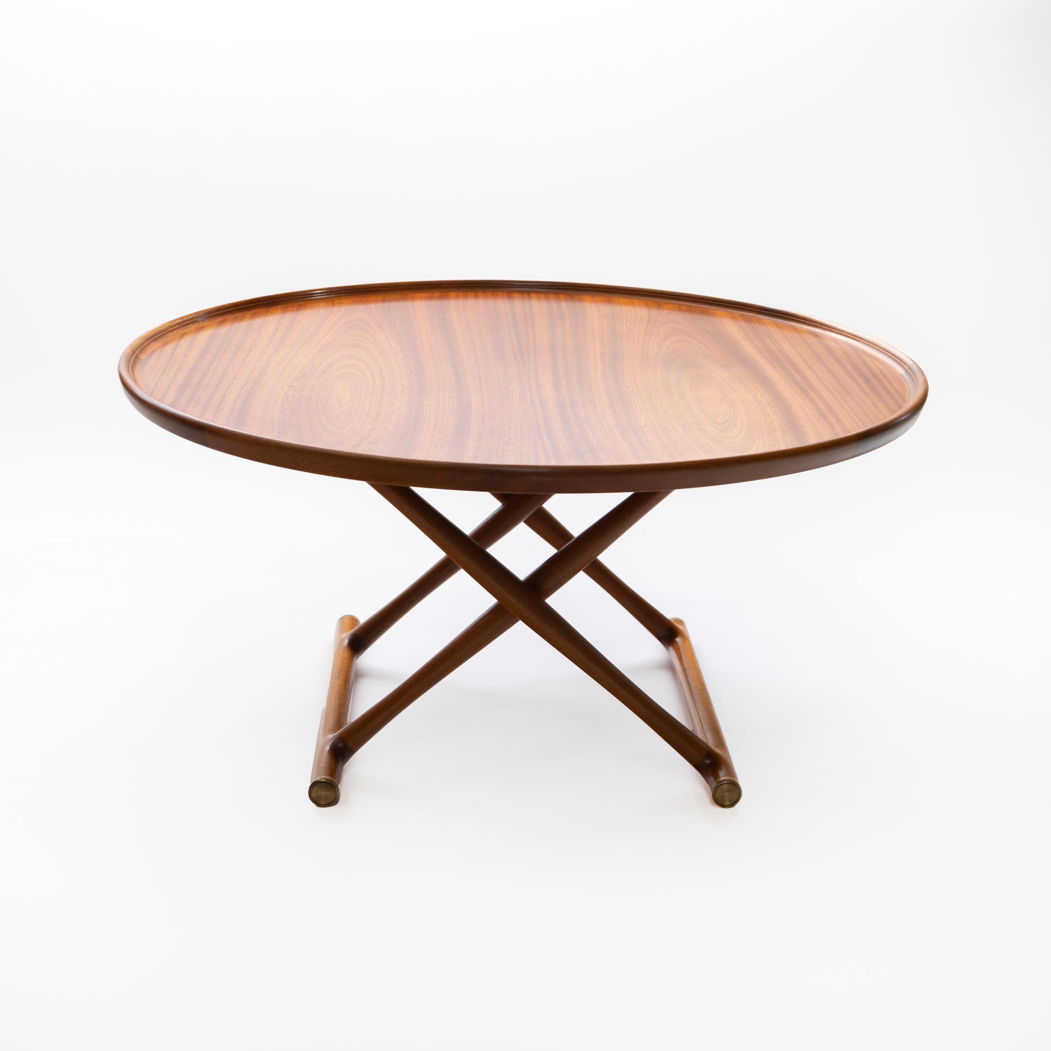 Mogens Lassen. The 'Egyptian Table' is a foldable coffee table crafted in mahogany, showcasing a beautiful grain pattern and a beveled edge tabletop. The cross-shaped base not only provides stability but also adds an elegant touch, finished with