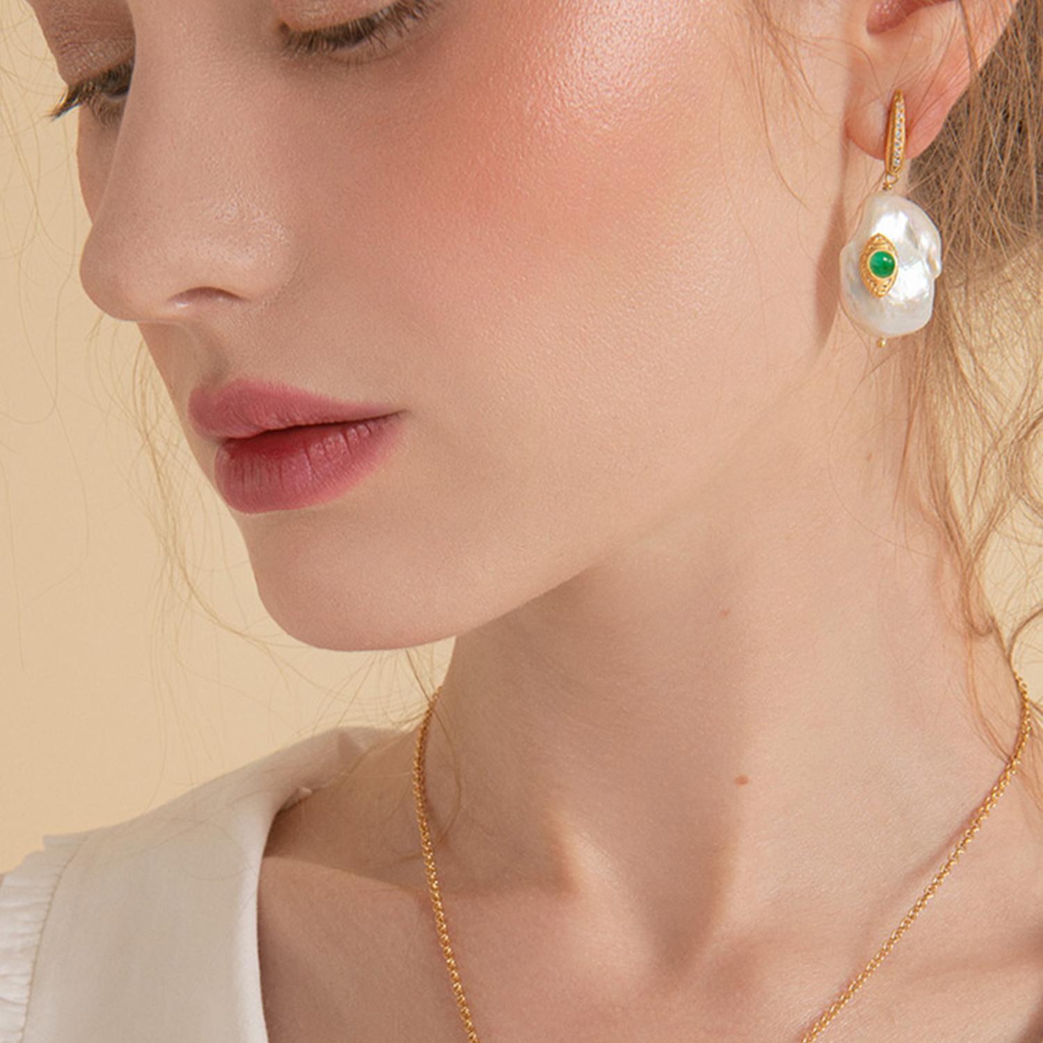 'The Eye' earrings by Vintouch are handcrafted from 18-karat gold-plated silver featuring vibrant green emeralds that are bezel-set in an eye-looking element inspired by Egyptian Eye of Horus, symbolizing protection. The dainty pearl is embellished
