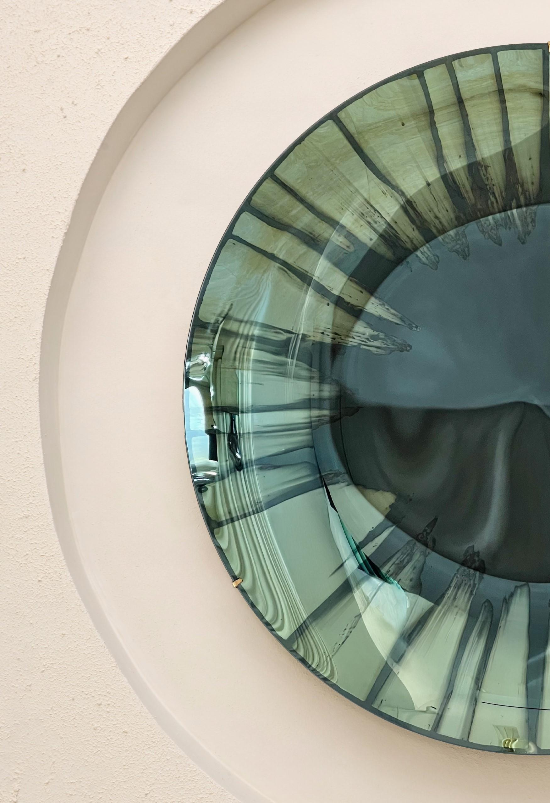 Concave Mixed Technique Mirror.
Ø97 cm  Depth: 7 cm  Thickness: 6 mm 
Colour: Green  Hanger: Brass


The EYE OF THE UNIVERSE: This collection explores different techniques in glass and presents innovative approaches to mirroring, challenging the