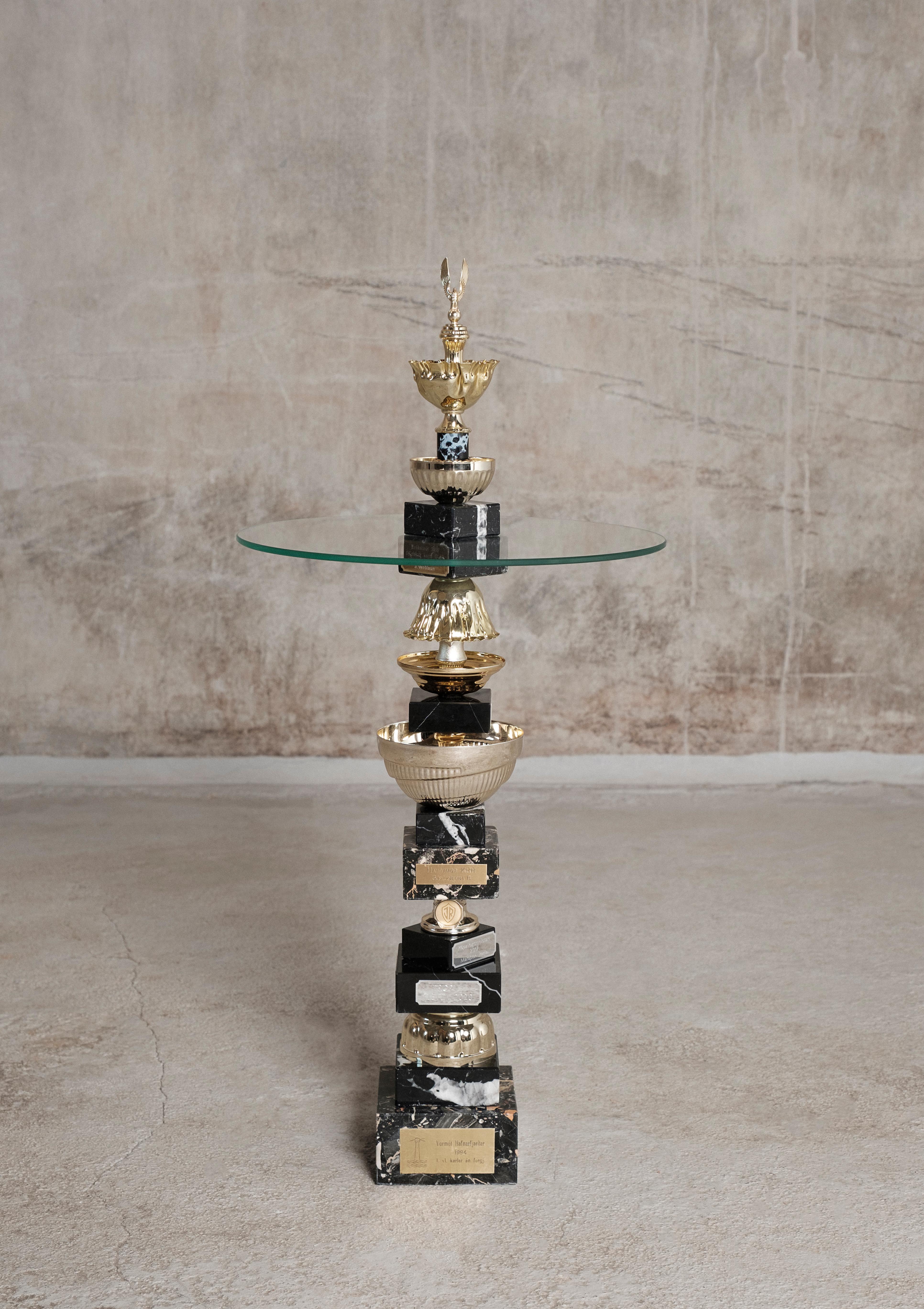 The Falcon table by Flétta
Dimensions: 87 x 62 cm
Materials: gold, black marble

Trophy is a collection of tables, lights, flowerpots and shelves made of old trophies collected from athletes and sports clubs in Iceland. Trophies are a part of