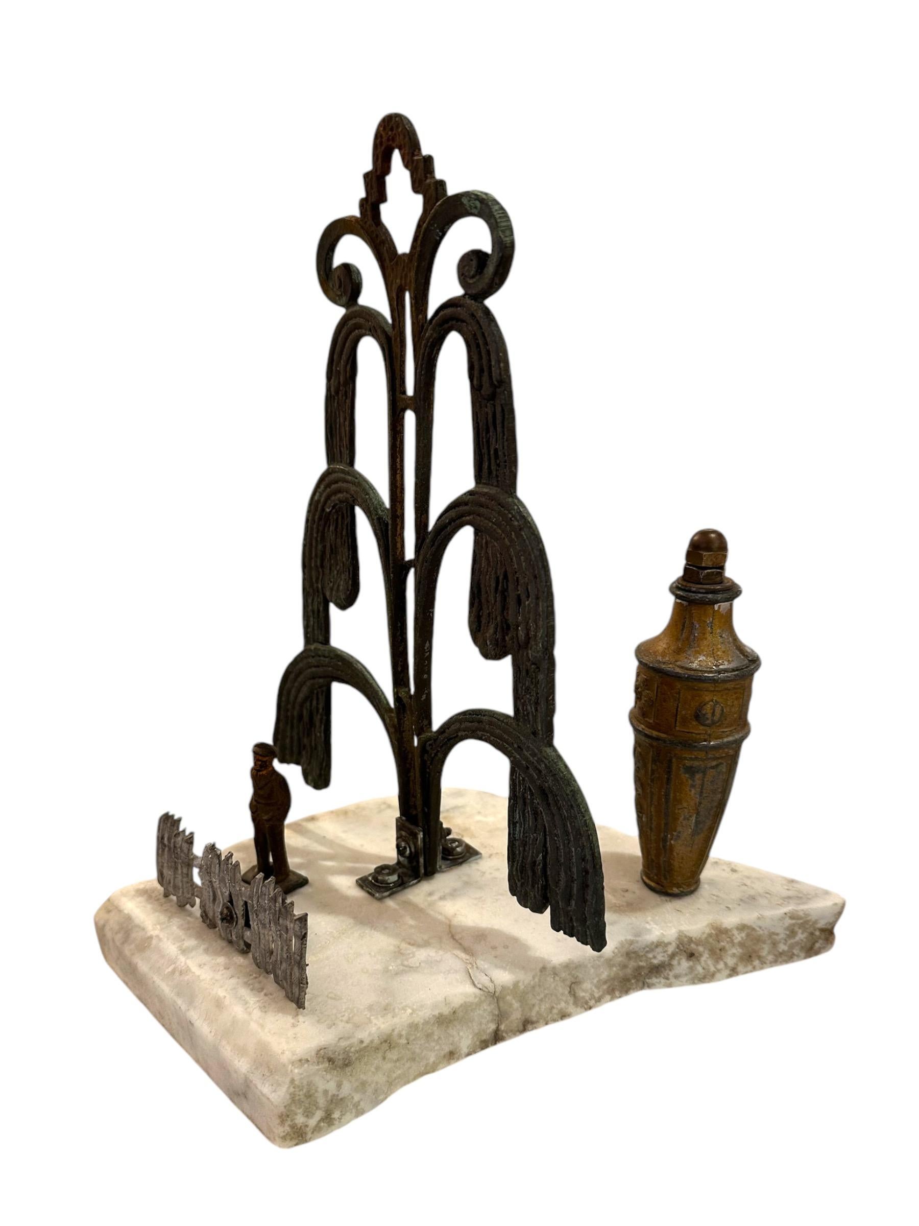 Self-taught artist John Seubert, AKA John Dolly, uses objects he uncovers as he rehabs older homes in Chicago. An ornate decorative metal piece is the focal point forming a cascading tree.  A small figure stands behind an artist cast pewter fence