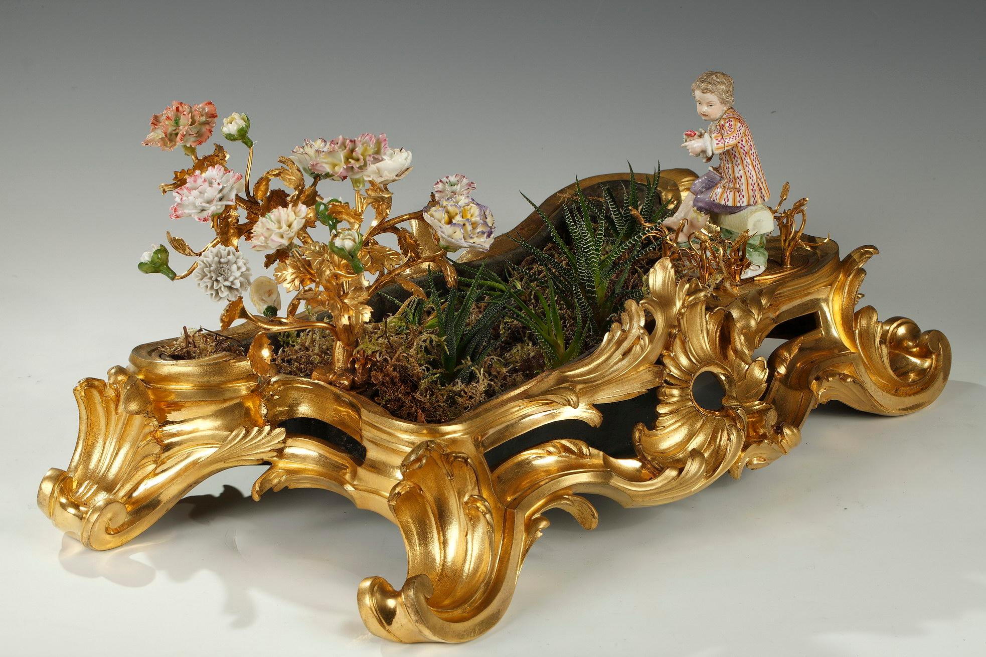 Charmante jardinière Rocaille d'époque Louis XV en bronze ciselé et doré, festonnée d'un décor asymétrique de feuilles d'acanthe et de rinceaux, et d'une coquille ajourée en son centre. Un bouquet en bronze doré et des fleurs en porcelaine