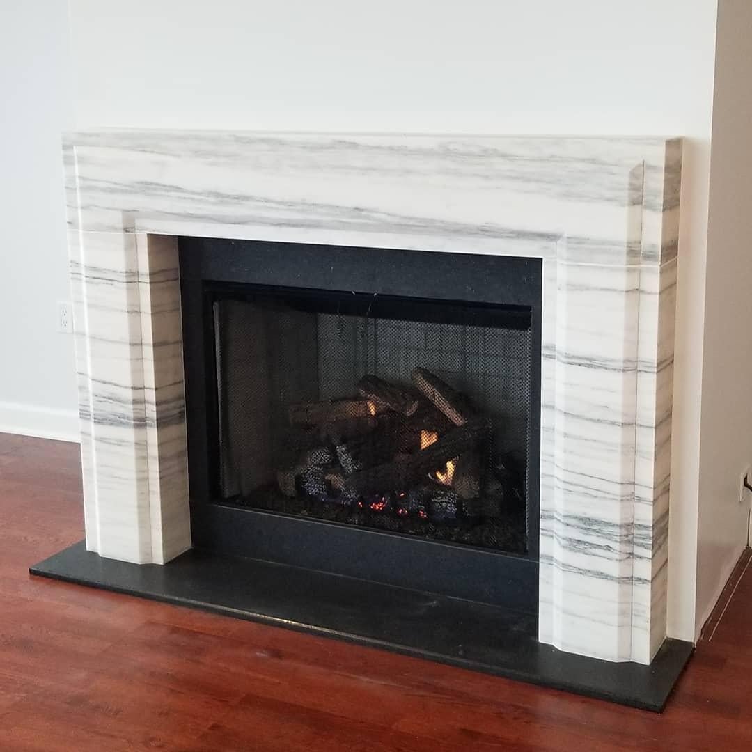 La cheminée en pierre de Gerherty présente un design moderne suffisamment simple pour s'intégrer dans de nombreux décors différents. Sa forme générale est rectangulaire, avec une section surélevée qui suit les pieds et le linteau, avec un léger