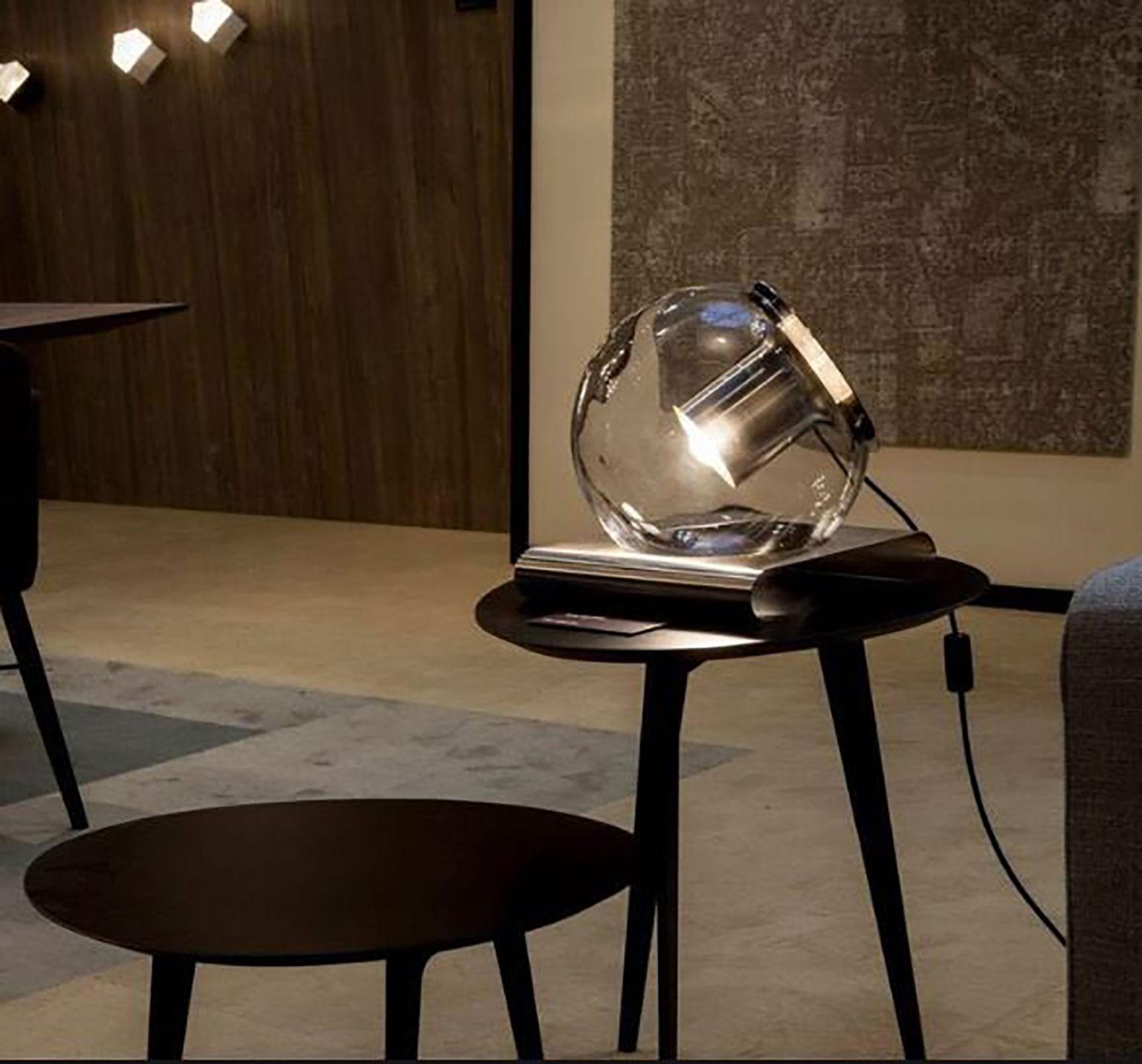 Die Tischleuchte Globe wurde von Joe Colombo für Oluce entworfen. Es handelt sich um ein einfaches und ansprechendes Design aus mundgeblasenem Glas, das mit Hilfe eines internen Metallreflektors ein bemerkenswertes Raumlicht erzeugt. Der gedrehte