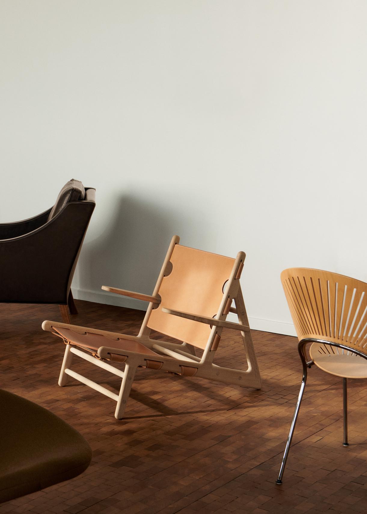 Der Hunting Chair ist einer der auffälligsten Stühle von Børge Mogensen, der 1950 entworfen wurde. Von der Seite betrachtet, fällt vor allem die starke diagonale Neigung der vorderen Sitzkante auf, die nur 30 cm über dem Boden liegt. Der Hunting
