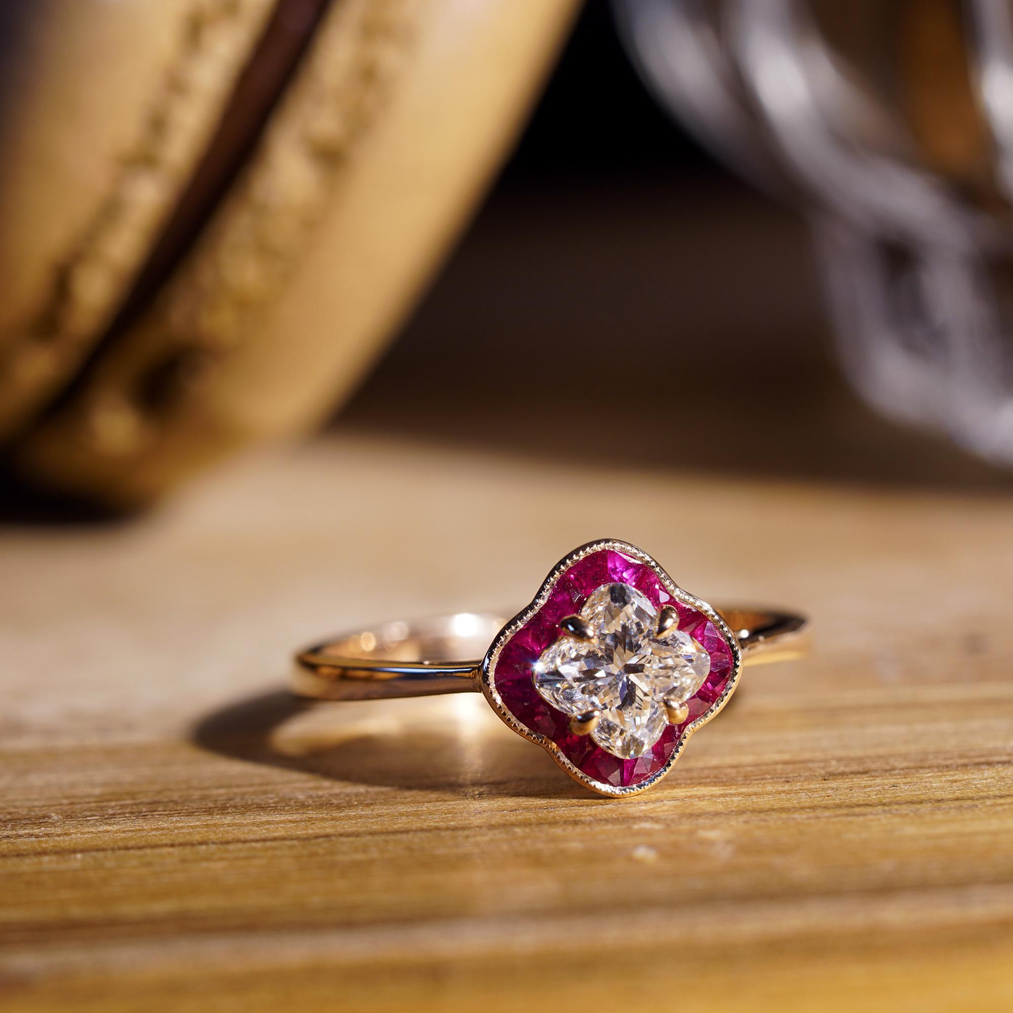 This delicate halo diamond and ruby engagement ring featuring a certified 0.07 carat lily cut diamond in prong set surrounded by French cut rubies. The ring is a classic choice with a modern twist! If you’re looking for an engagement  ring with a
