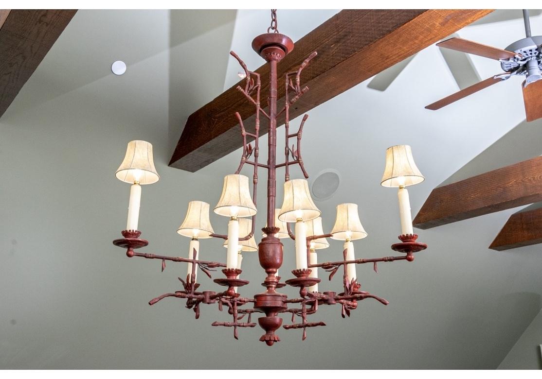 Painted bronze chandelier by Paul Ferrante in antiqued rust red tones. Branch or Bamboo form with leaves and 9 lights with scalloped bobeches, lined faux skin shades, and faux wax drip candle sleeves. The standard with an urn form base and shaped