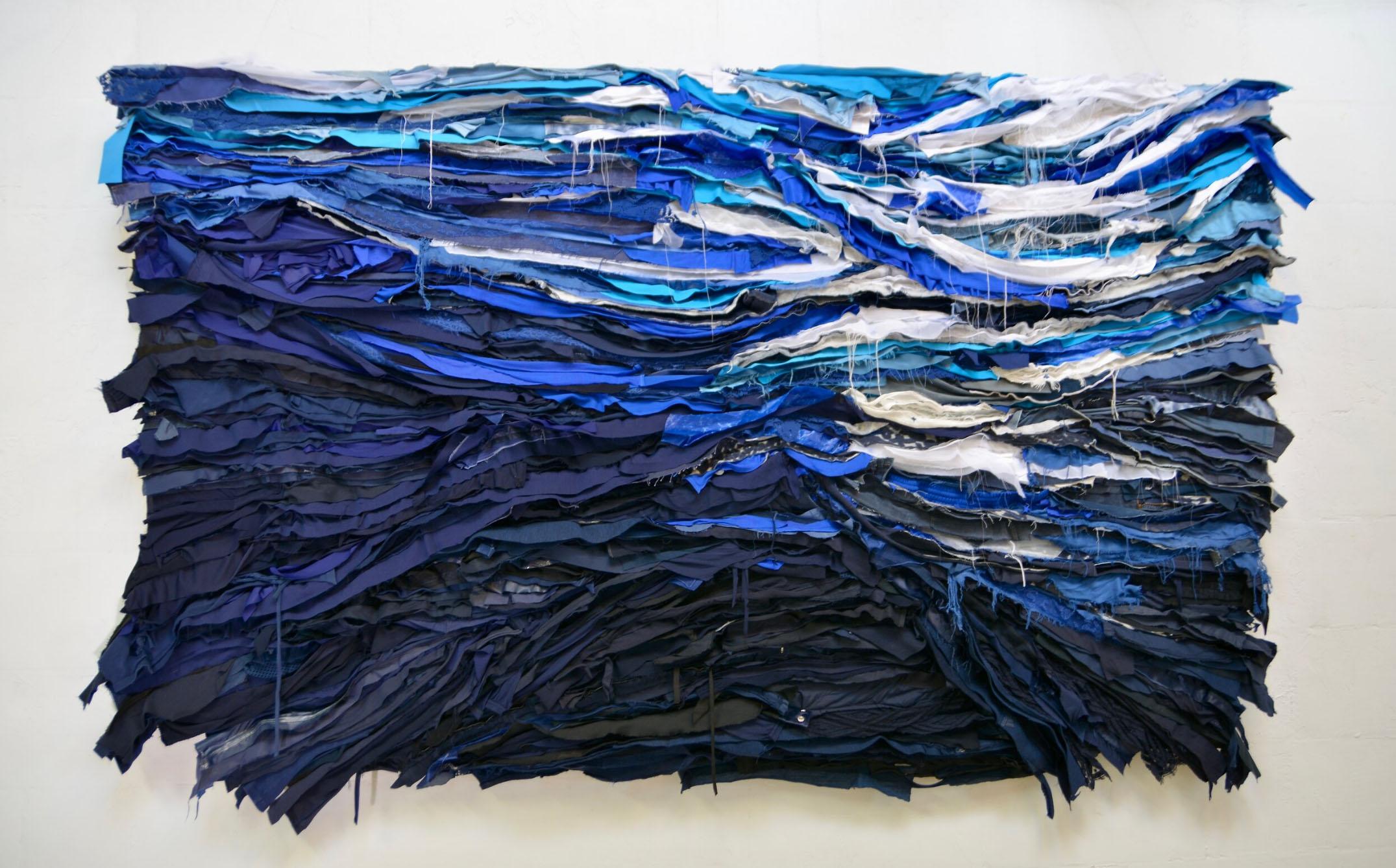 Femke van Gemert uses discard textile to create her sustainable soft wall art reliefs. This work is made of the clothing leftovers and reveals some details of the clothing, such as zips, buttons and labels. The work is devoted to the sea
