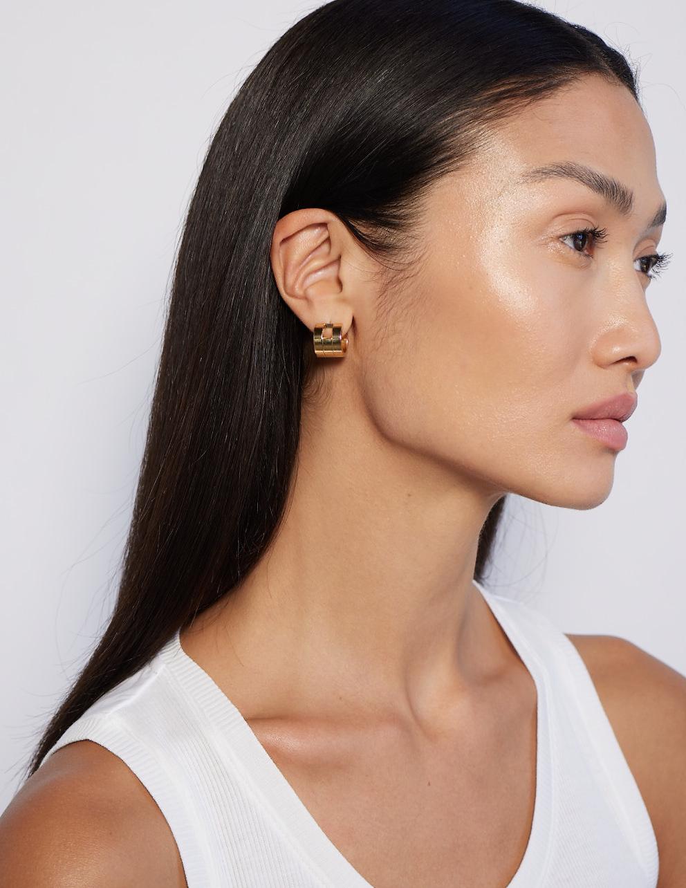 The Margueritte Earrings: Compact in scale but bold in presence, the Margueritte Earrings reinterpret the sculptural language of the Margueritte Cuff into a pair of chunky, architectural hoops. Crafted in solid 18K gold, each hoop is built from