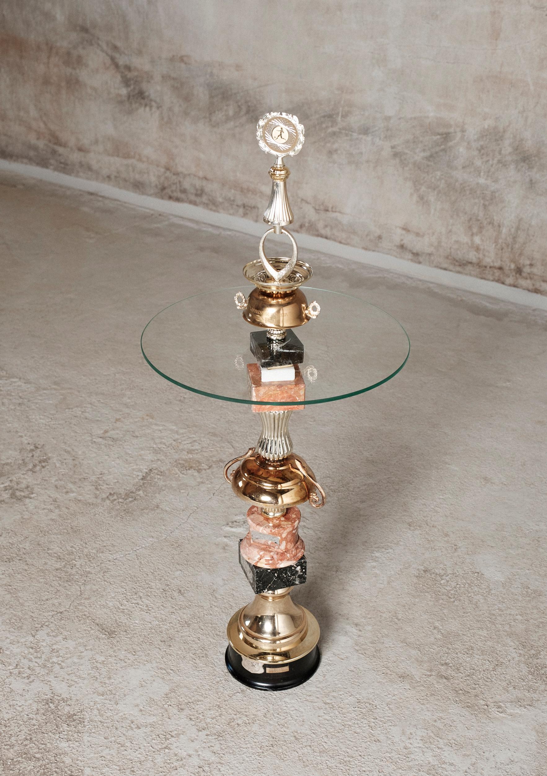 The Olive Wreath Table by Flétta
Dimensions: 87 x 62 cm
Materials: Gold, silver, pink marble

Trophy is a collection of tables, lights, flowerpots and shelves made of old trophies collected from athletes and sports clubs in Iceland. Trophies are