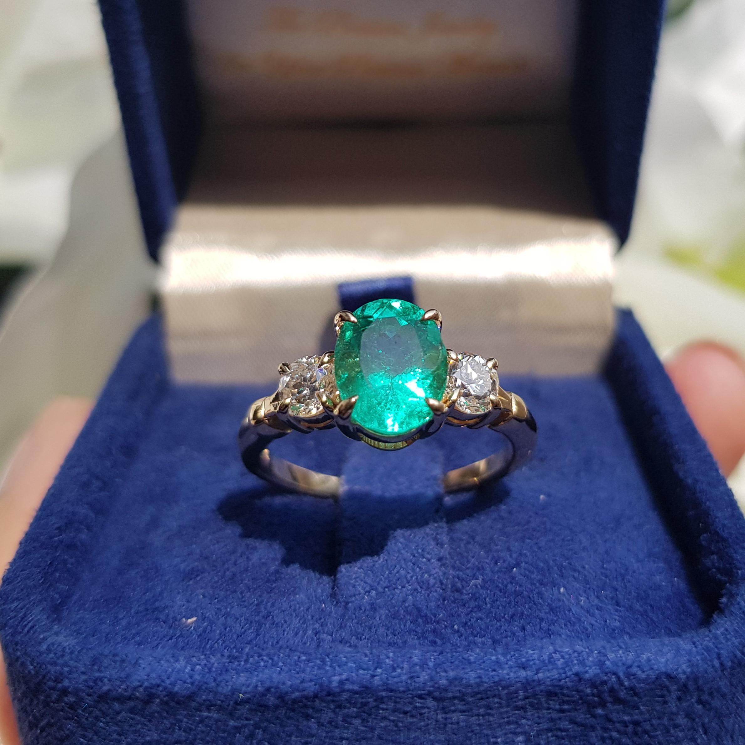 Sophisticated and stunning, this petite emerald and diamond ring is a classic three-stone design crafted in solid 18K yellow gold. A vibrant 2.03 carats oval-cut emerald gemstone is accented by two round old-cut diamonds, for a look that never goes