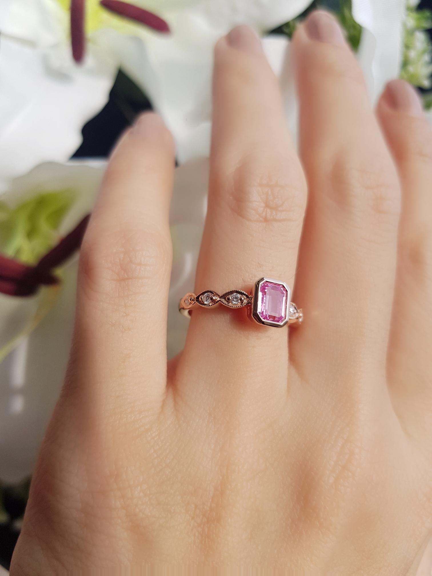 This gorgeous pretty ring is beautifully set with an emerald cut natural pink sapphire and round diamonds on shoulders. The intense pink sapphire is in bezel setting. The diamonds each set into an elongated marquise create a unique detailing to this