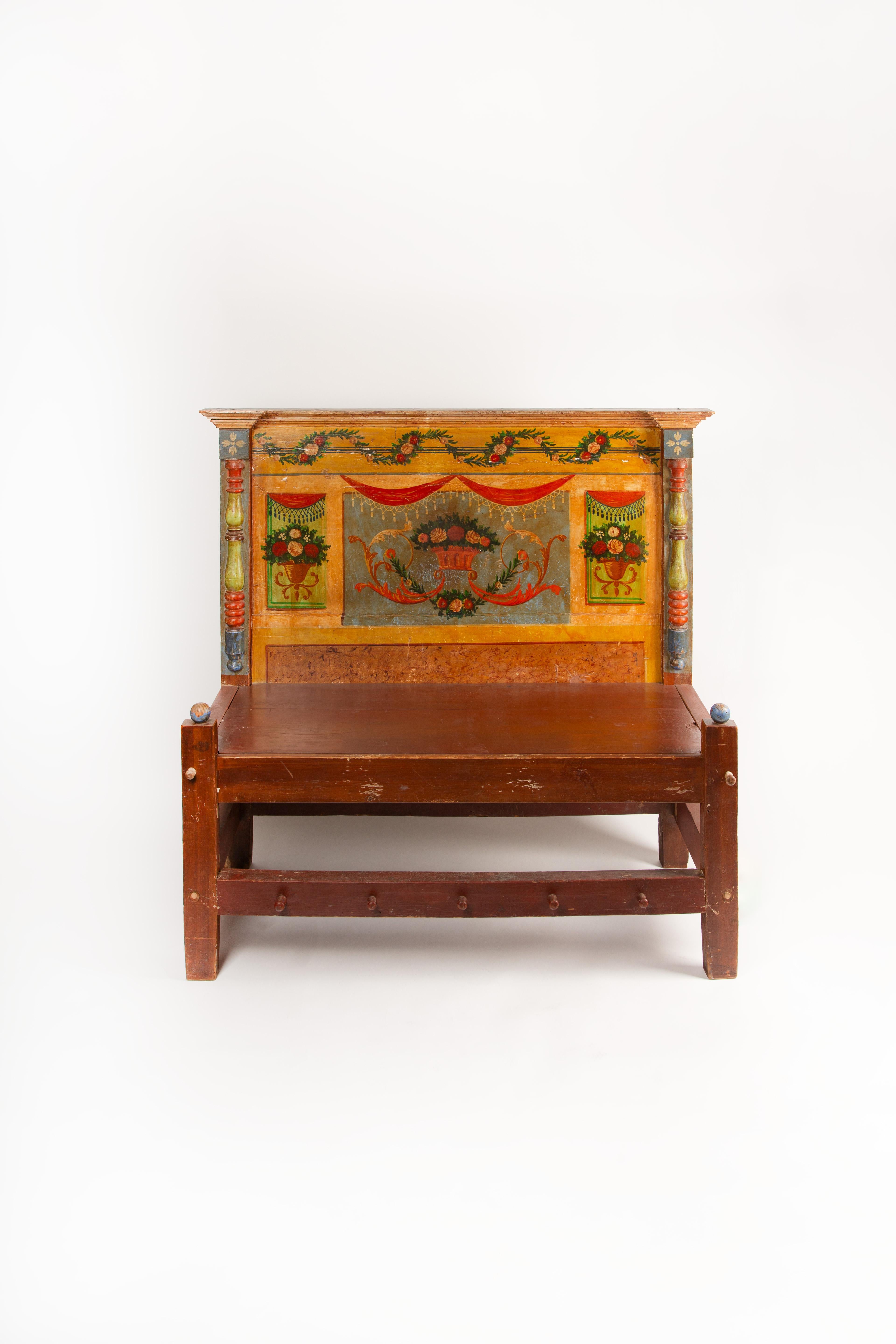 This charming 19th-century Venetian bench is a vibrant example of Italian folk artistry, featuring an elaborately hand-painted backrest adorned with neoclassical motifs. Floral garlands, urns, and scrolling foliage frame a central basket of flowers