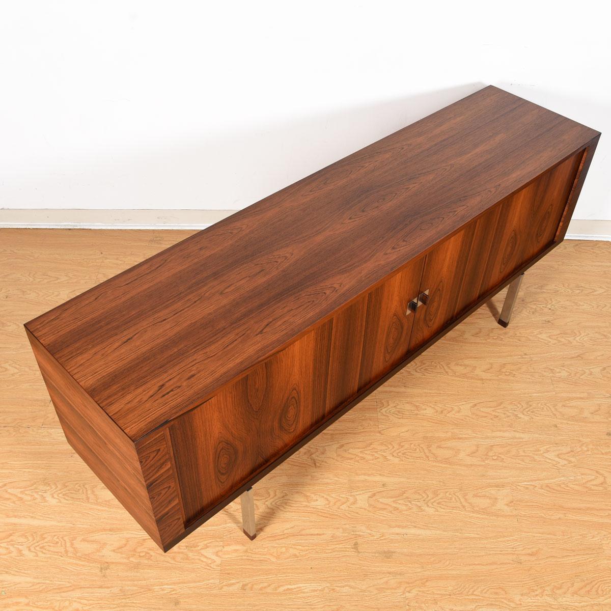 Long sideboard with brilliant Brazilian rosewood by Hans Wegner for Ry Mobler. Patterned figuring throughout the case and on the tambour doors of this piece. Rosewood capped chrome legs support the sideboard, which is paired with rosewood accented