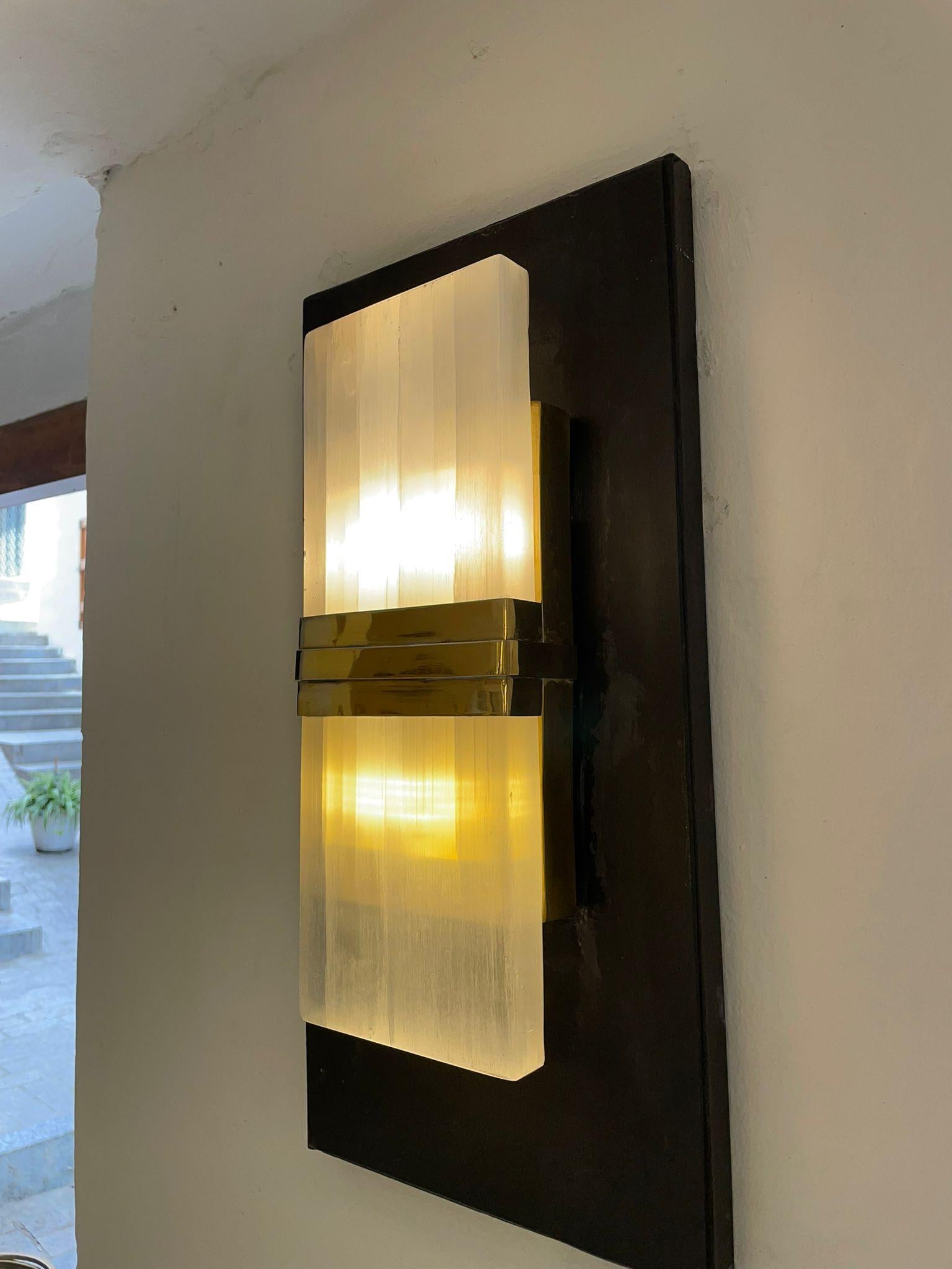 This  wall light is a meticulously handcrafted piece, combining solid brass with natural selenite crystal. The design highlights the crystal’s vertical striations, contrasted by the sleek horizontal brass structure — a refined play of symmetry and