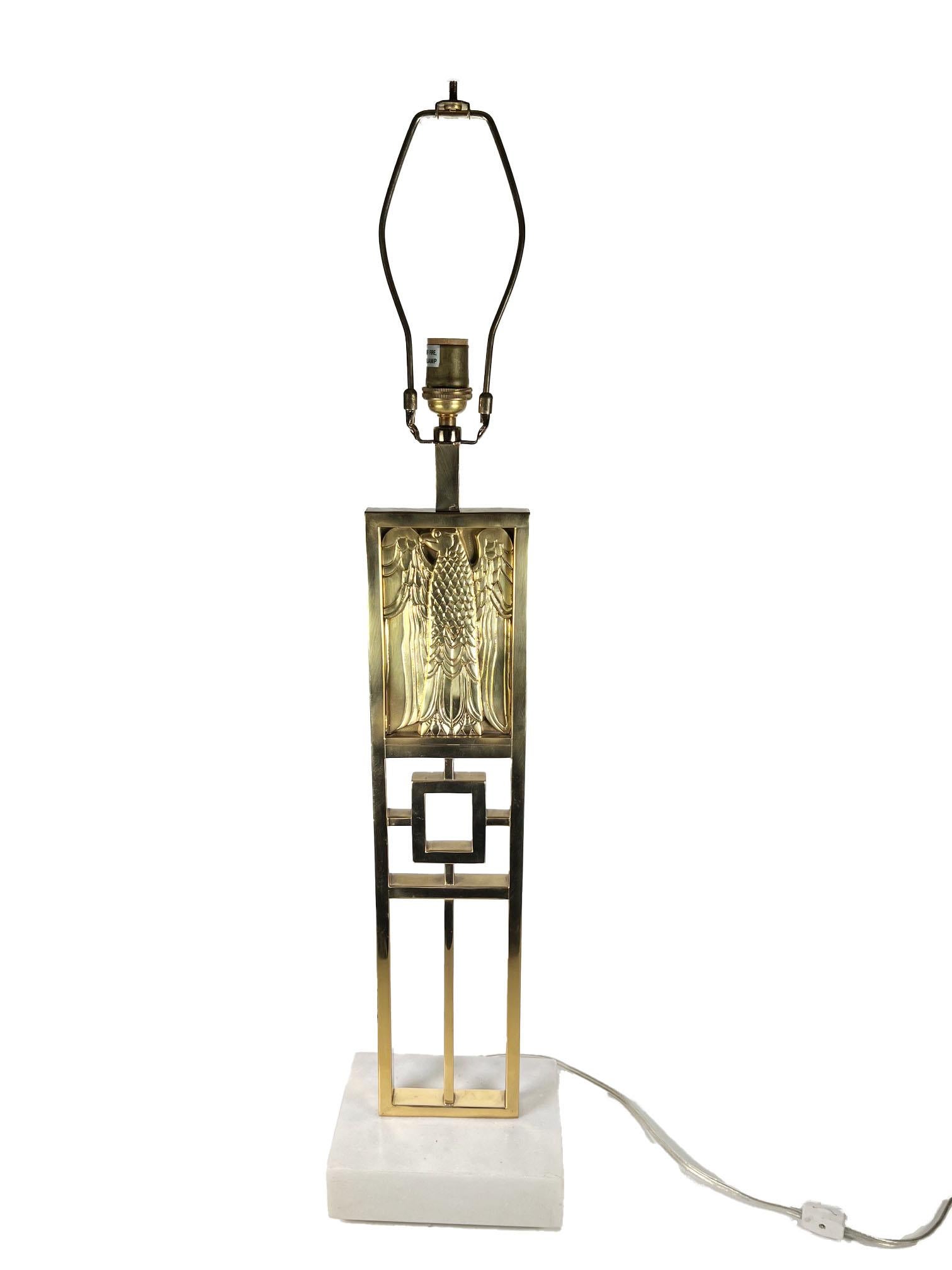 Lampe de table de style continental, fabriquée en laiton massif et montée sur une base en marbre de Carrare reposant sur quatre pieds élégants. Le design présente un motif d'aigle en relief, symbolisant la force et la grandeur, d'inspiration