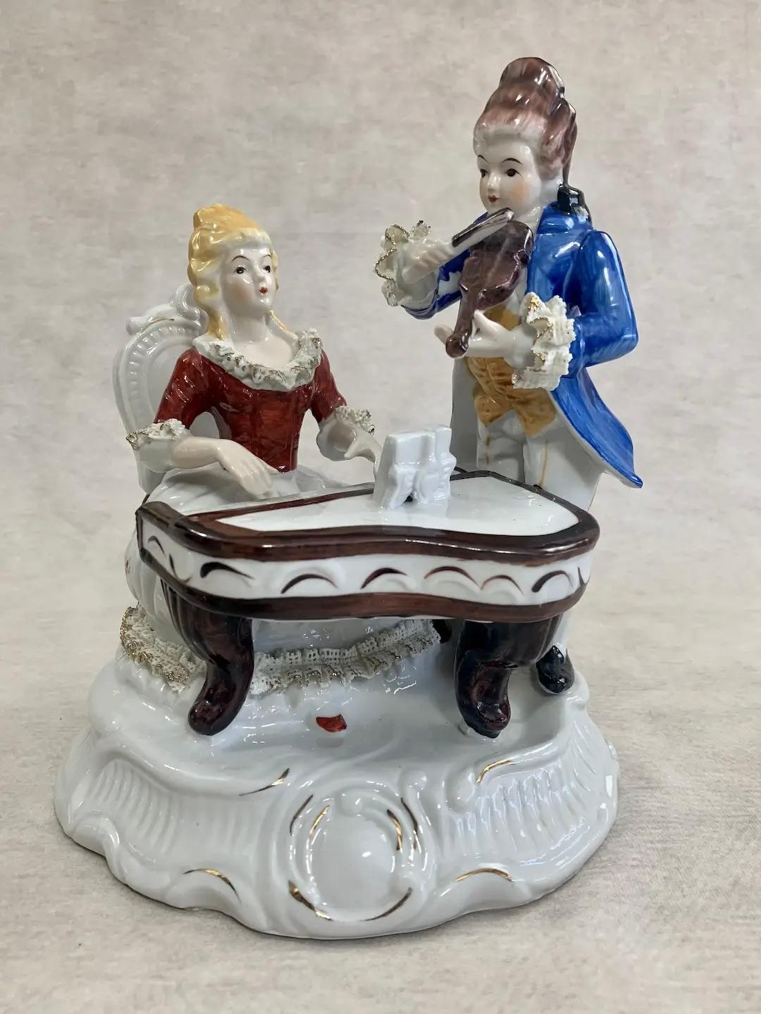 Vintage porcelain figurine evoking the style of the highly sought romanticism of the Victorian era depicting a scene of two classical musicians, a pianist and violinist, engaged in a duet. Each figure is beautifully dressed in traditional formal