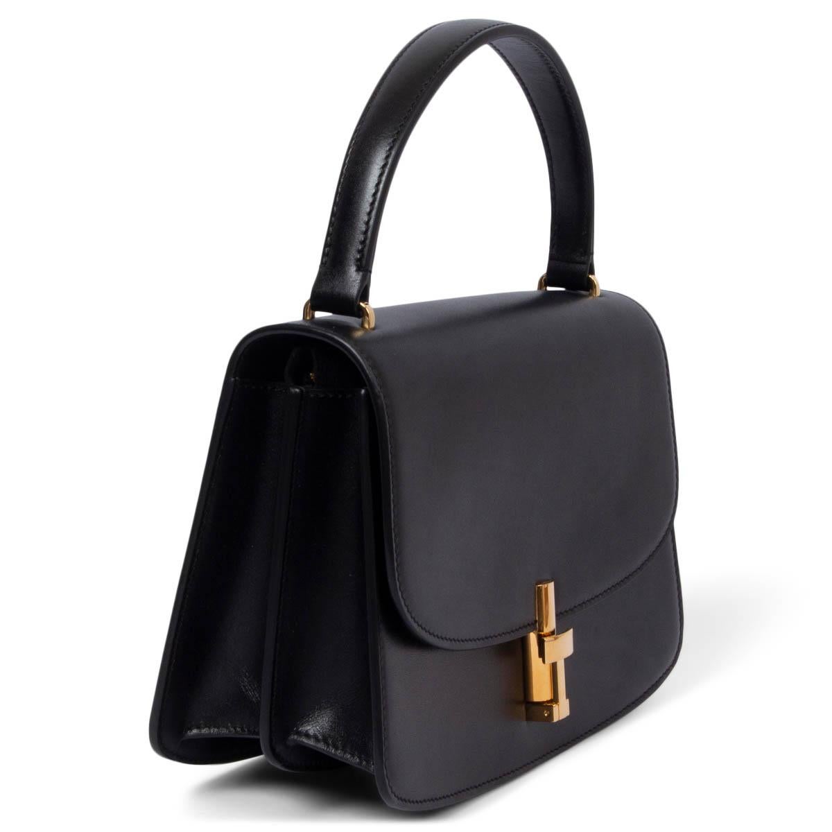 100% authentic The Row Sofia bag in black smooth calfskin. This style has a streamlined silhouette with a curved base, a fixed top handle, and a metal turn-lock closure in gold-tone metal. The design features a black leather lining, two internal