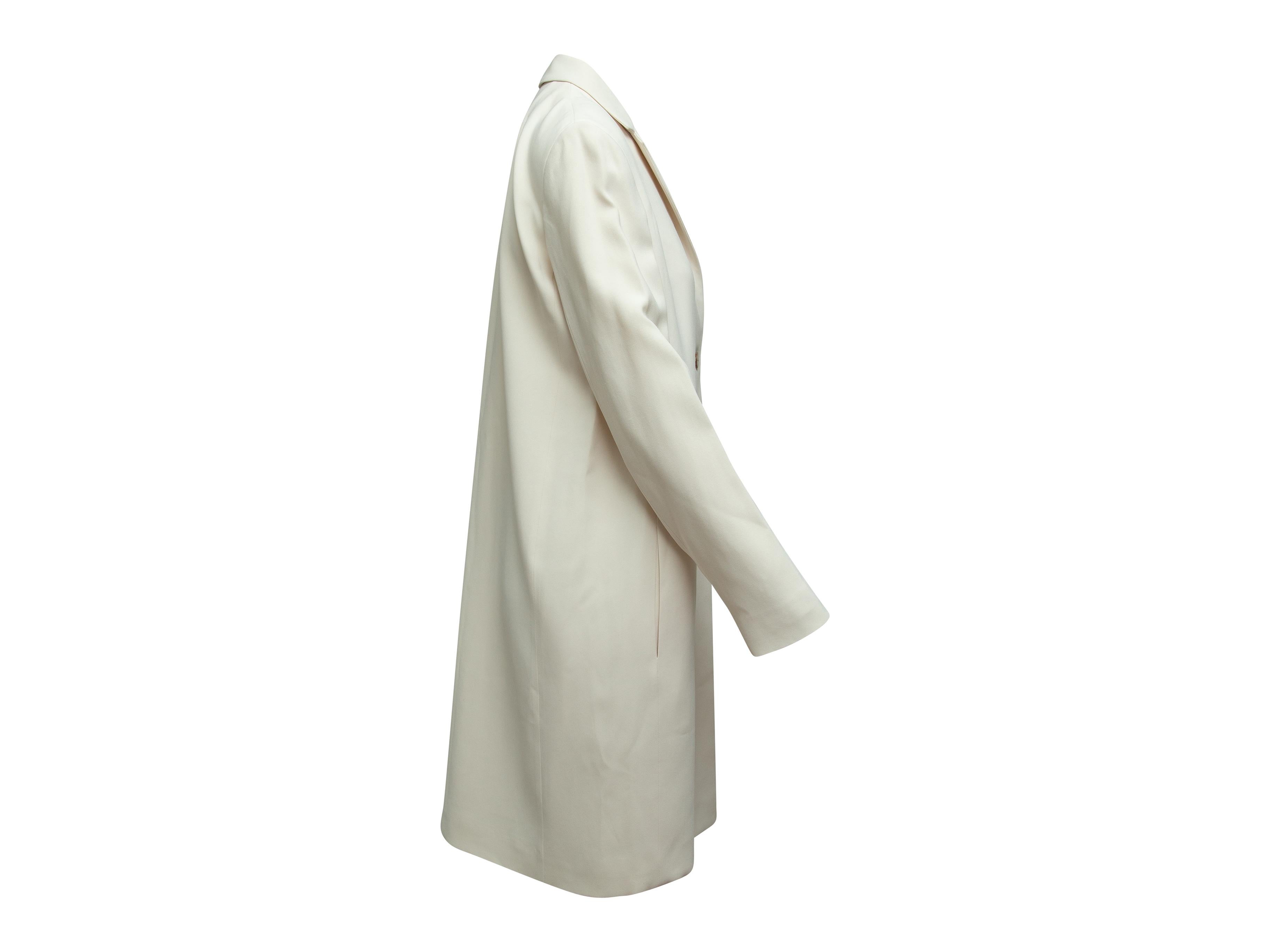 Product details: Cream long collared coat by The Row. Notch lapel. Dual slit pockets at hips. Horn button closures at center front. 42
