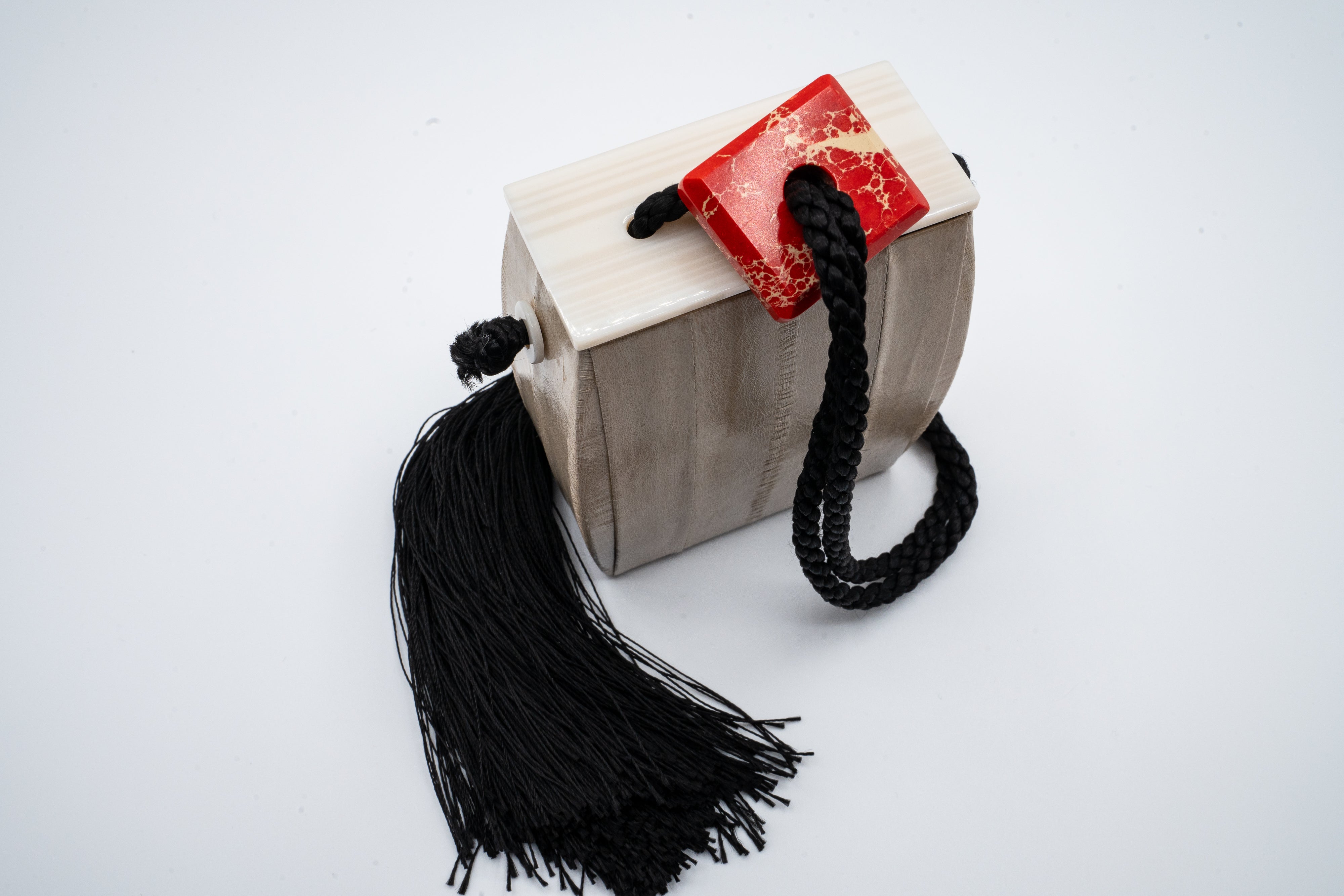From The Row's Spring 2018 collection, the Inrou bag reinterprets the traditional Japanese inro with a modern twist. Crafted in sumptuous beige eel skin, its smooth surface is beautifully accented by a sleek black tassel and a marble-like red stone