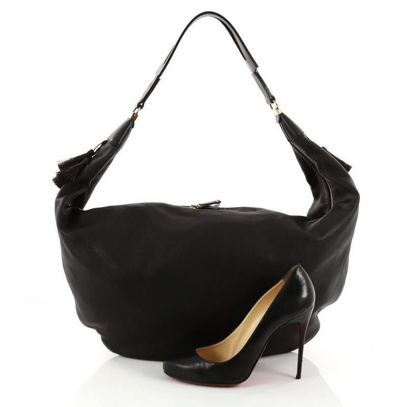 This authentic The Row Sling Hobo Leather 15 is a versatile and travel-friendly bag. Crafted in black leather, this chic bag features wide flat leather strap accented with horse tail hair tassels and gold-tone hardware accents. Its zip closure opens