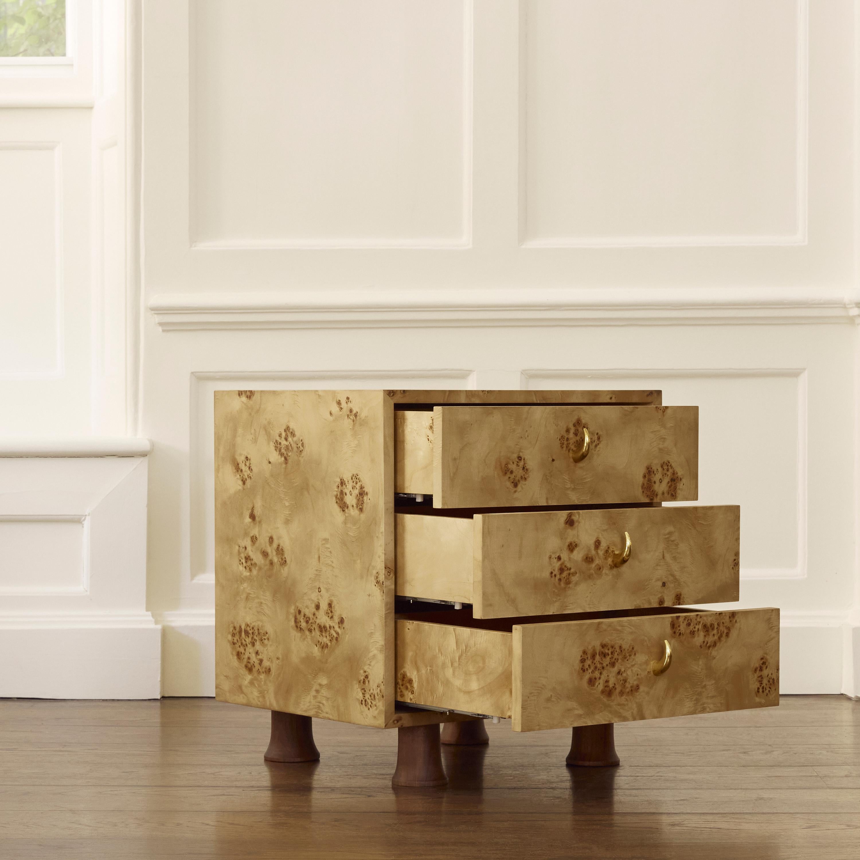 The Sable Bedside Table’s body is cut and constructed out of mappa burl, a wood veneer whose grains are peppered in natural contrasts of amber and hazel. The piece is finished with polished brass horn handles and propped by American black walnut