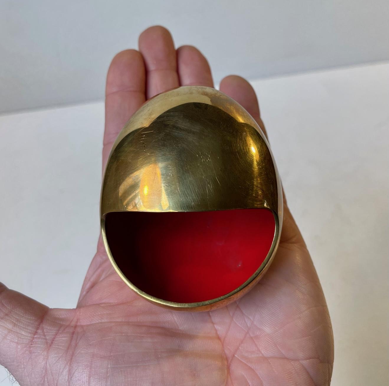 Iconic egg shaped Brass Ashtray with bright red interior enamel. It is called the smile and was designed by Hans Bunde and manufactured by Carl Cohr in Fredericia Denmark during the 1950s. Stamped Cohr, Denmark - to the base. It remains in beautiful