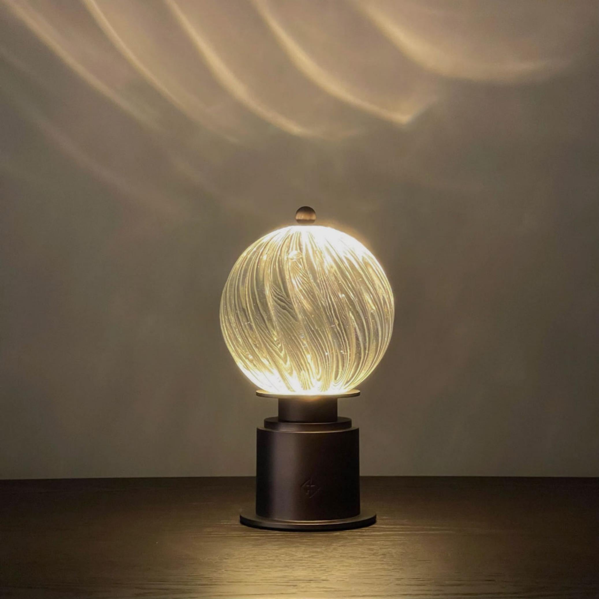 accentuate your home with the quietly-elegant lamp, created to evoke the swirling magic of a glowing globe. articulated with a solid glass spiral sphere and an anodized bronze base, the lamp is designed to accentuate your home with a sensuous