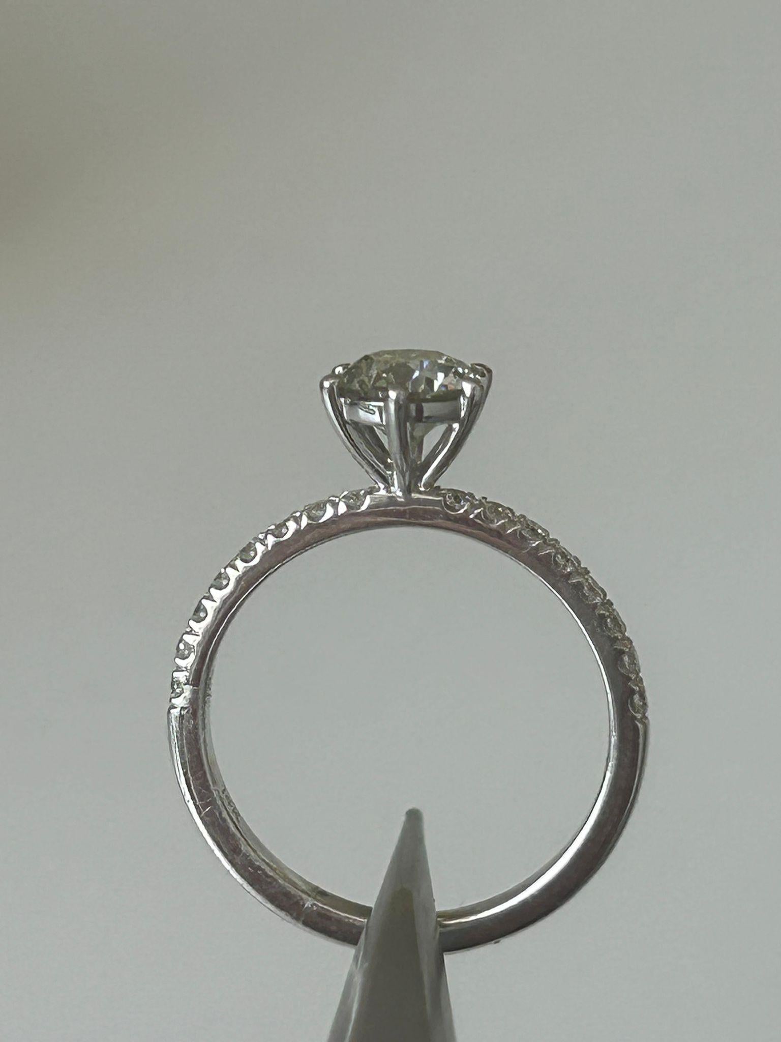 Im Mittelpunkt dieses atemberaubenden Rings steht ein brillanter Diamant im Rundschliff von 1.01 Karat, der zeitlose Eleganz und außergewöhnliches Funkeln ausstrahlt. Der zentrale Stein wird von 16 zart gefassten seitlichen Diamanten mit einem